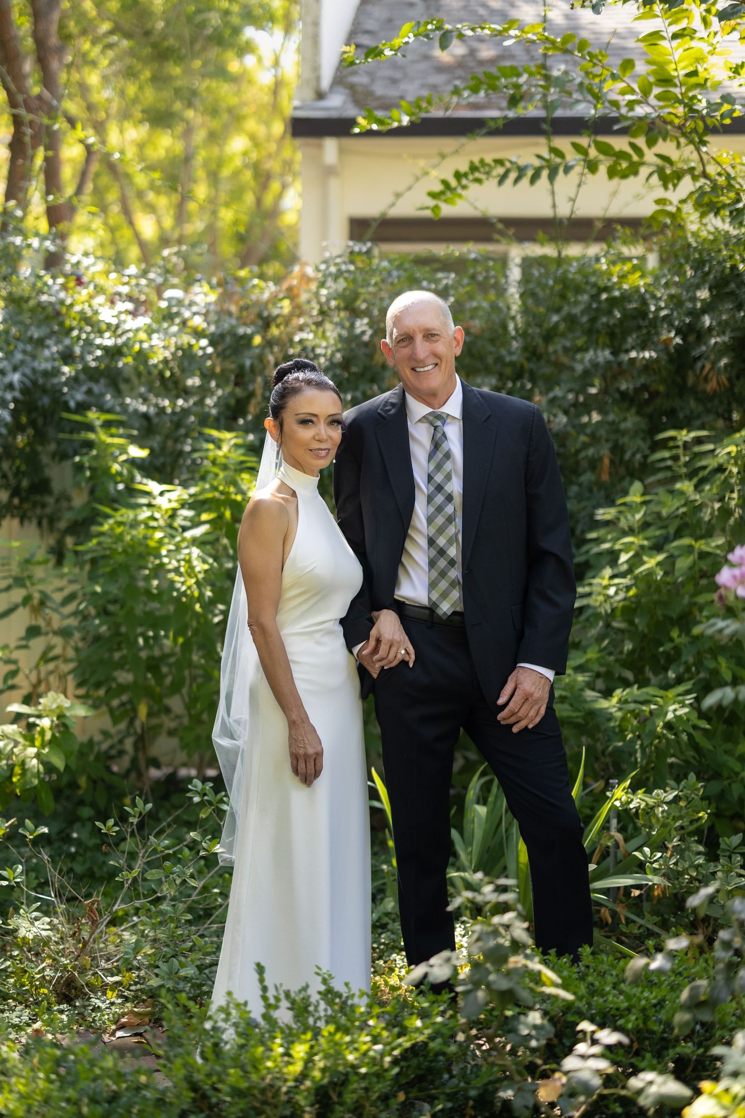 Wedding couple poses together in a lush garden setting with natural lighting.