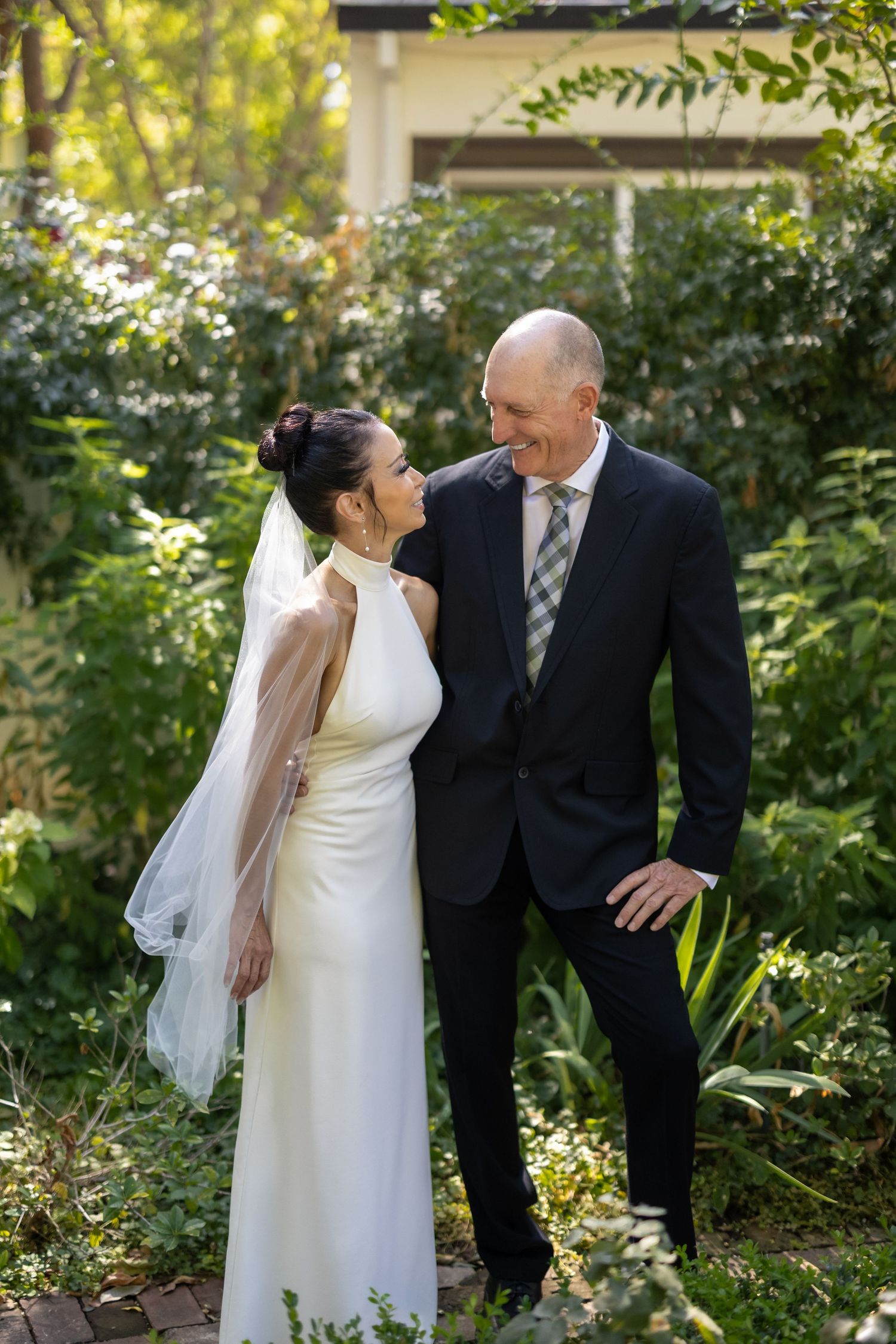Newlyweds share playful moments in lush garden setting.