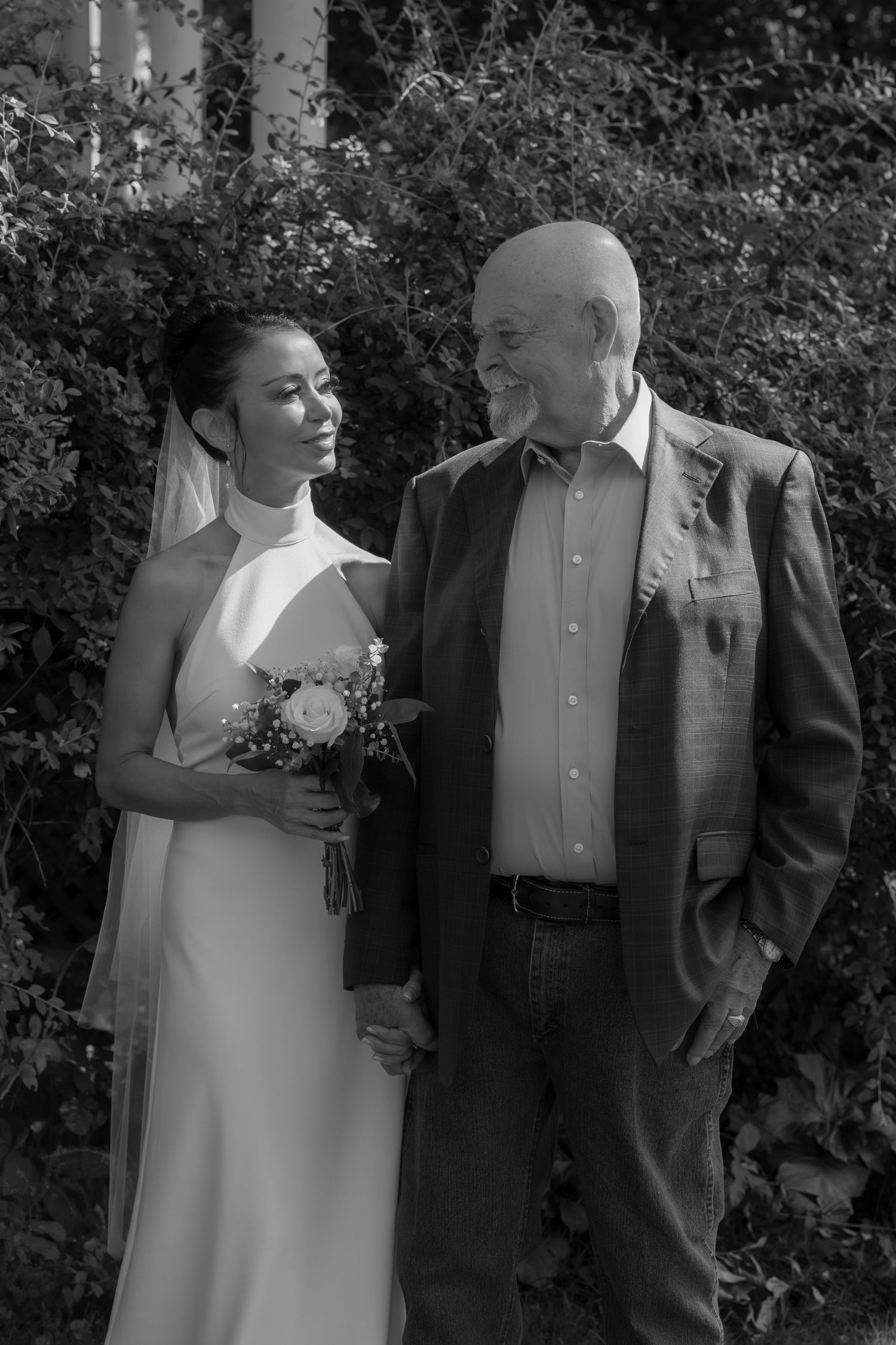 A couple shares intimate moments in formal attire against a garden backdrop.