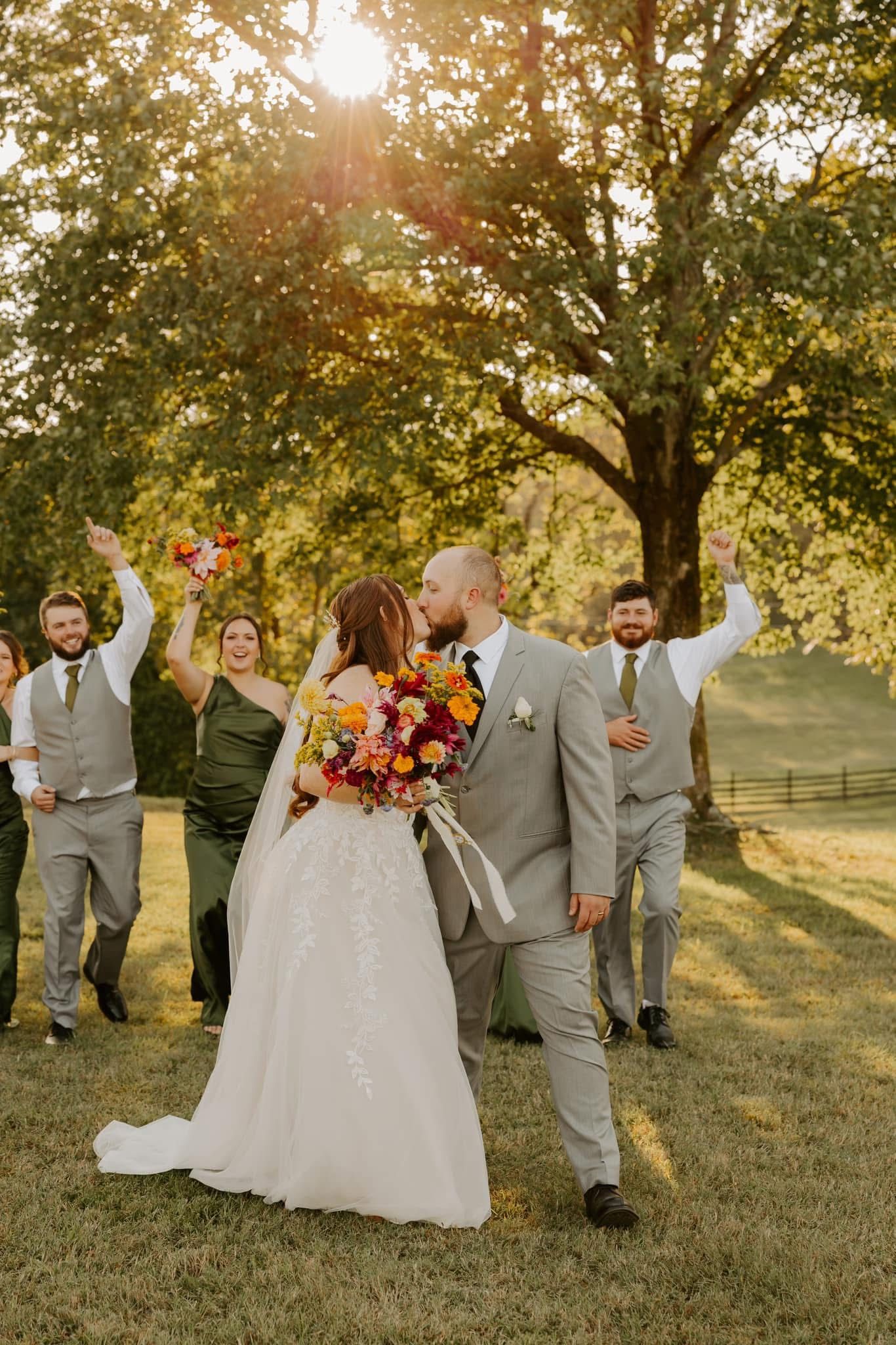 Wedding party celebrating outdoors with joyful poses under autumn trees.