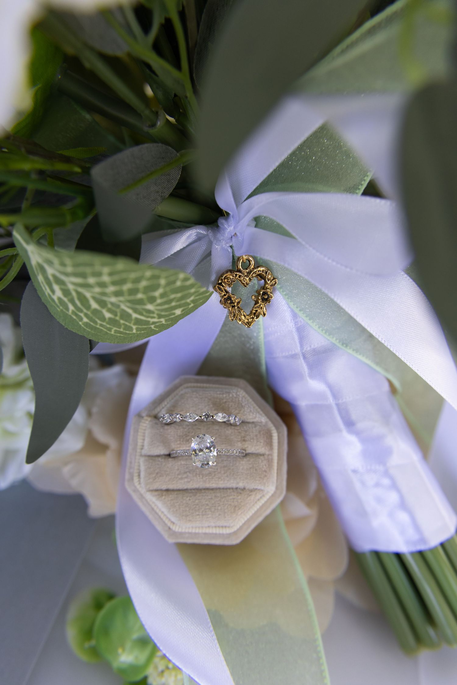 Wedding rings and jewelry displayed on white ribbon with greenery accents.