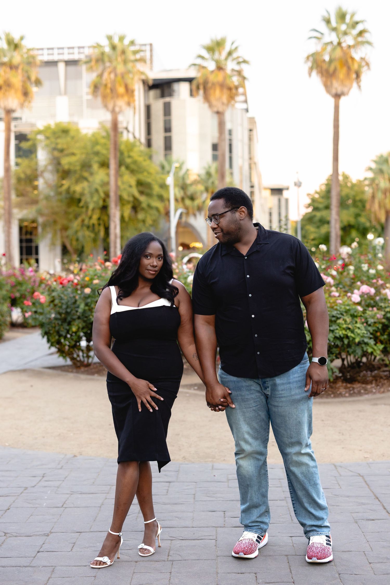 A couple strolls together through a palm-lined plaza with rose gardens.