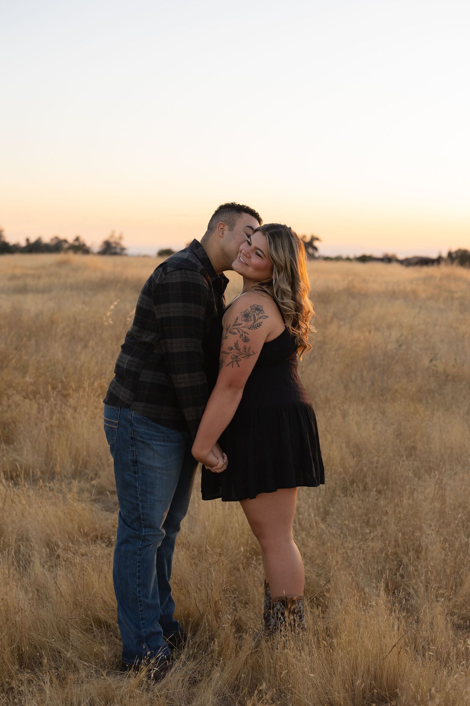 A couple embraces in a golden field during sunset.