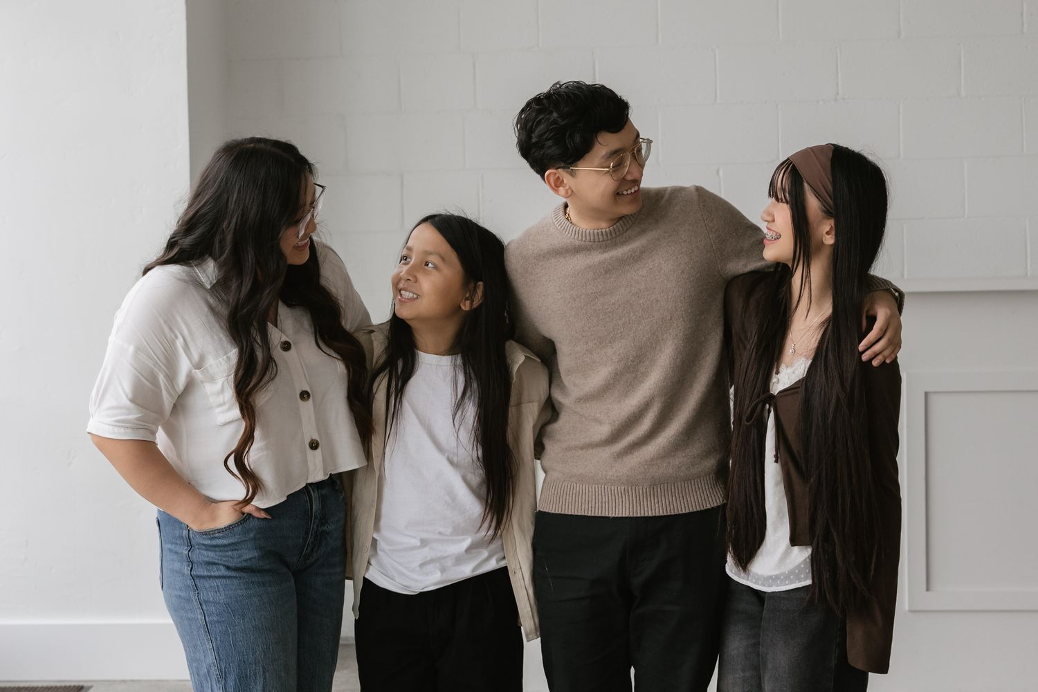 A group of people in casual attire laughing together against a white wall in a studio setting.