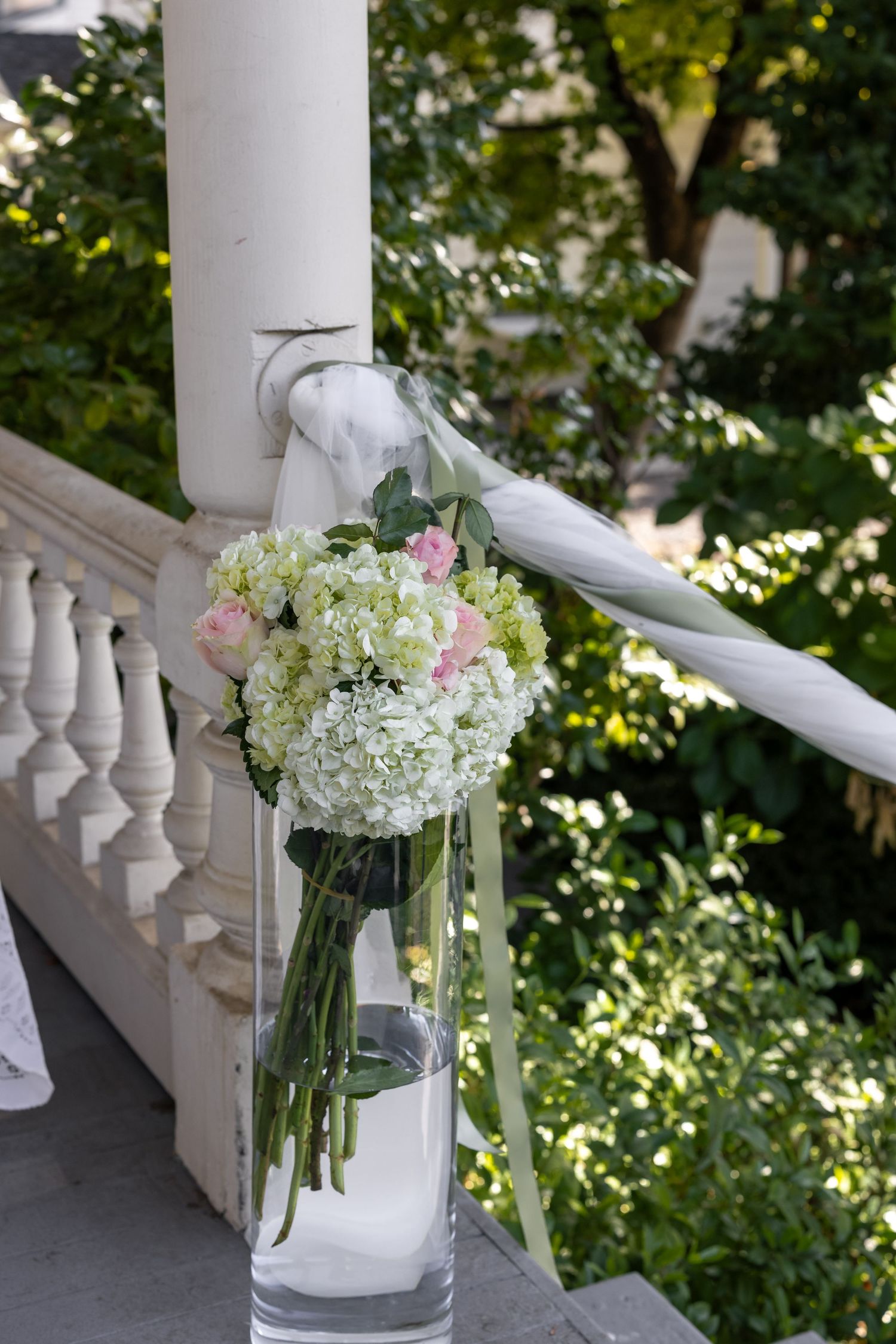Glass vases filled with hydrangeas and pink flowers decorate a white porch railing.