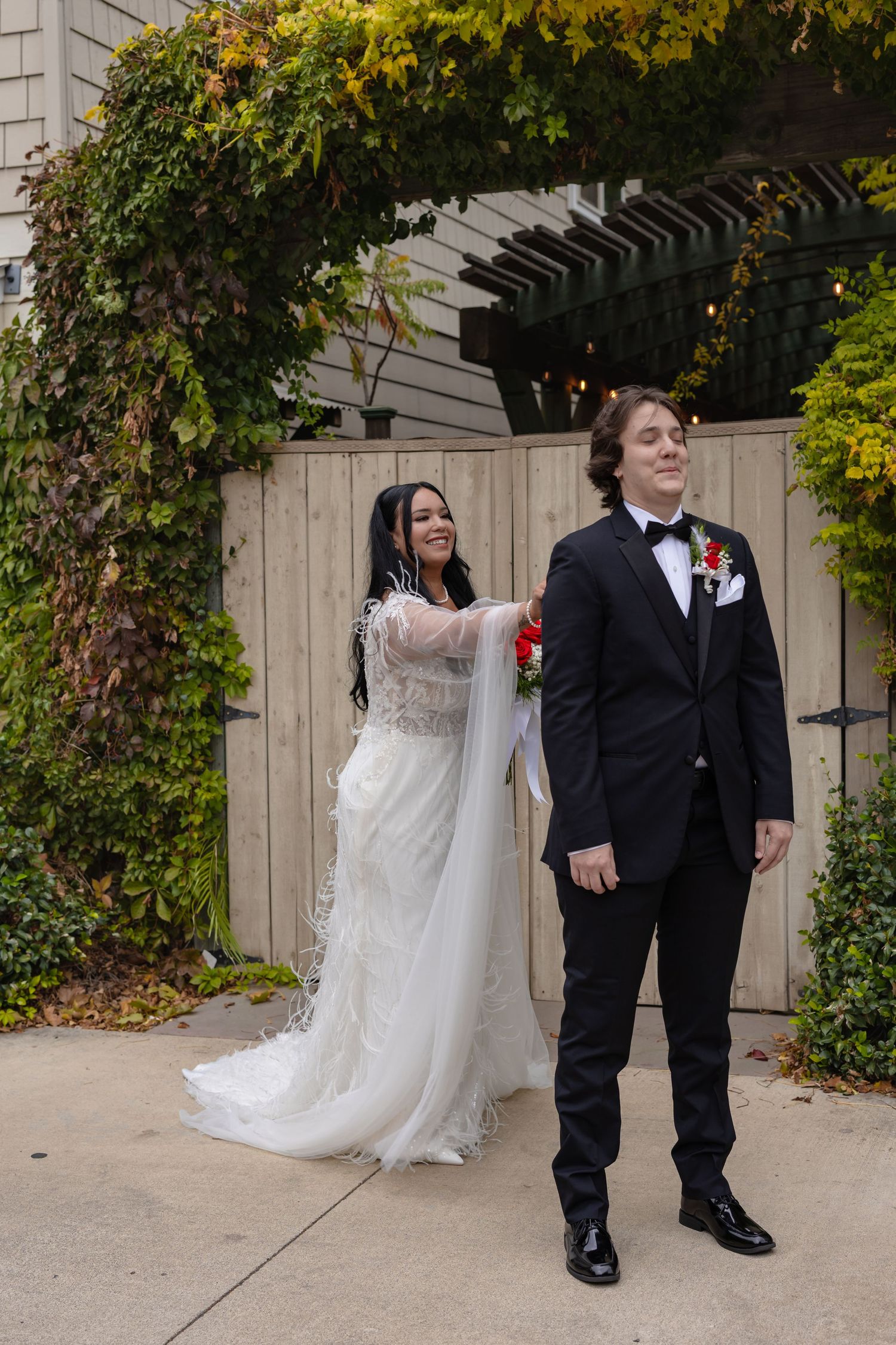 Wedding couple walking together outdoors along a garden path with vine-covered fence.
