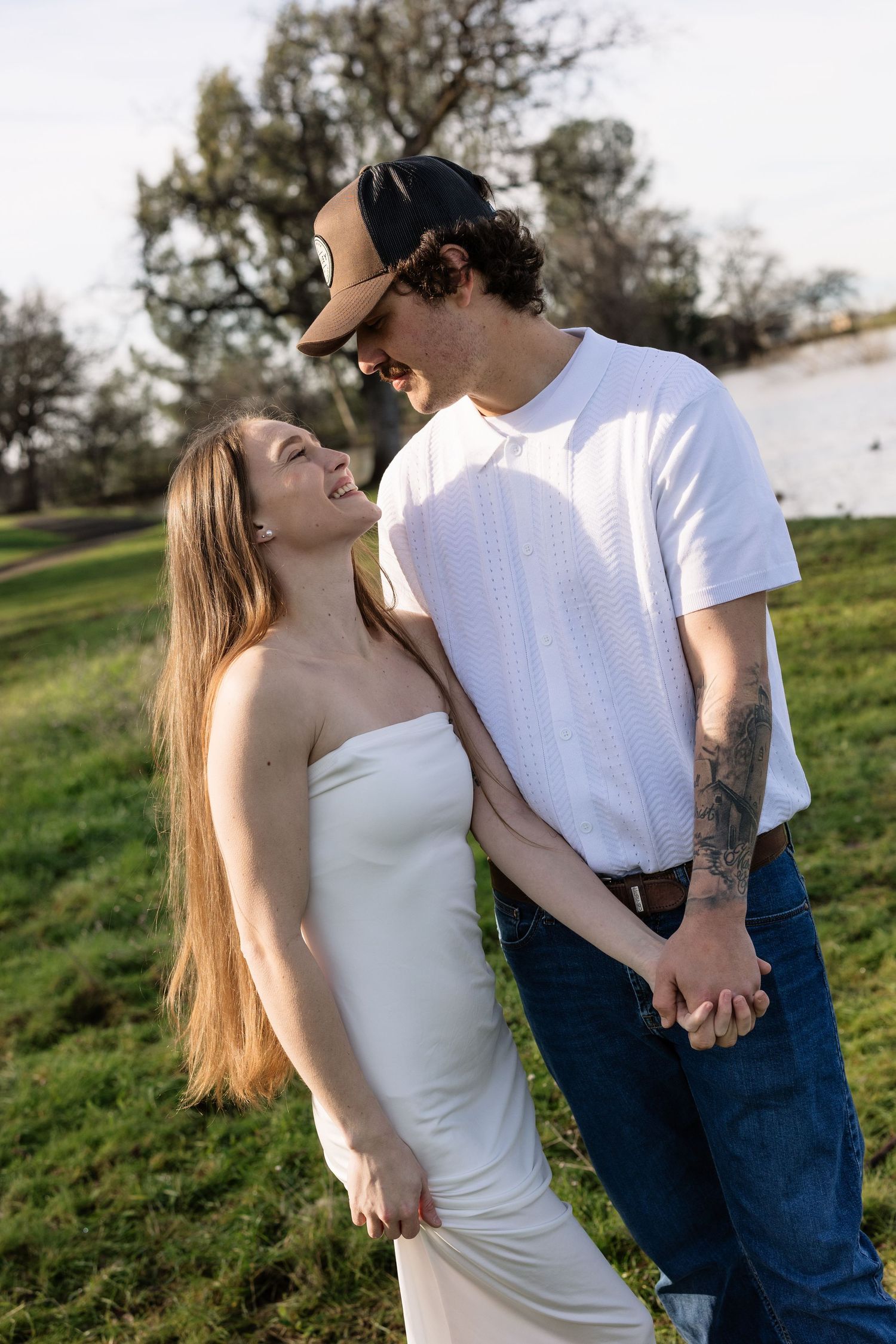 A couple sharing intimate moments outdoors on a grassy hillside in casual attire.