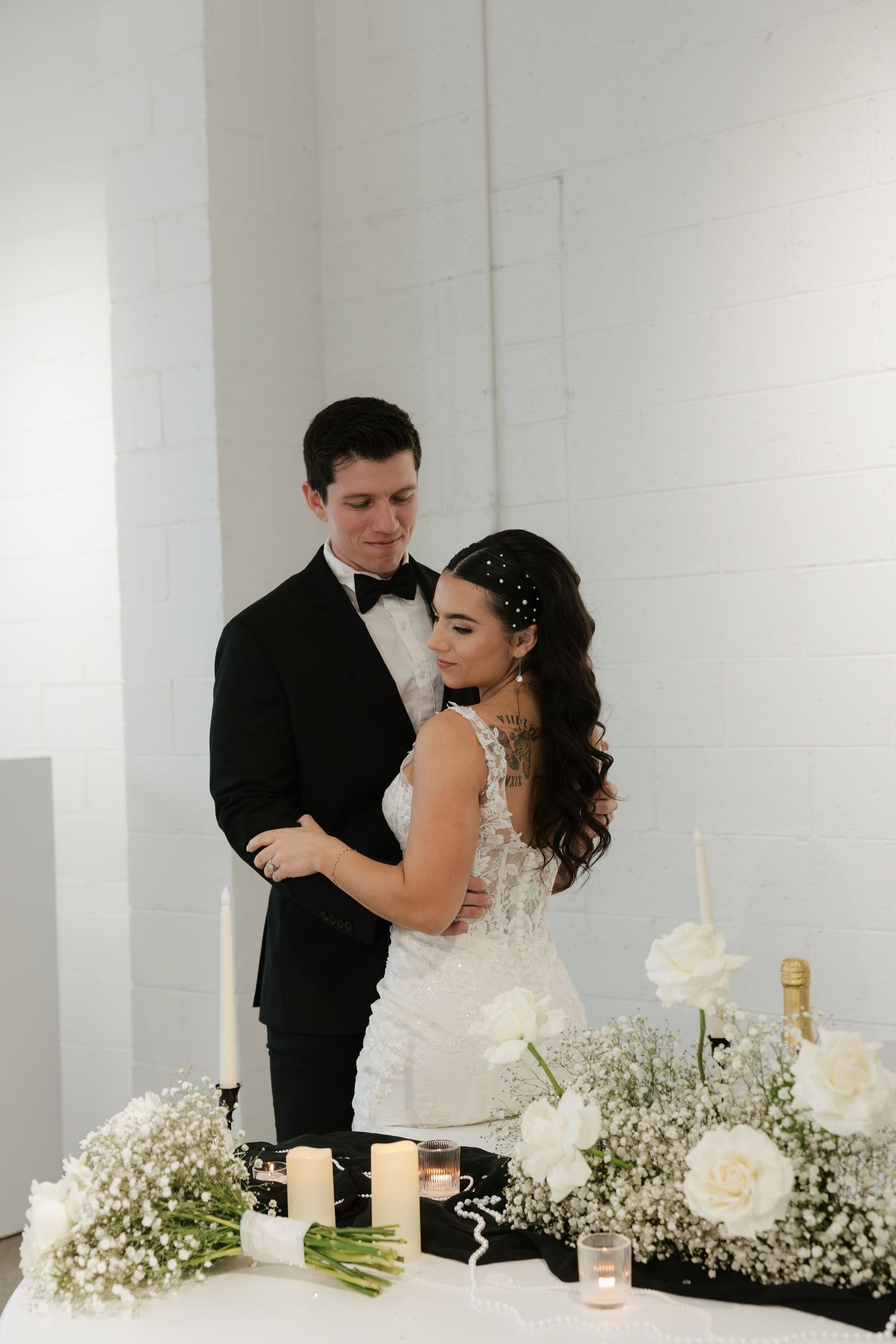 Newlyweds share an intimate moment at their reception table decorated with white roses and baby's breath flowers.