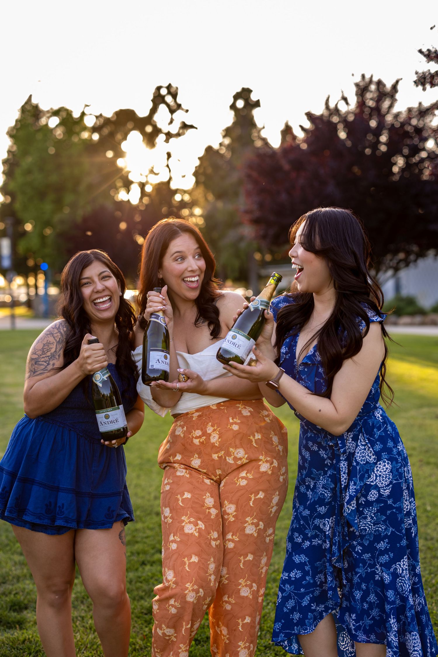 Friends in floral dresses laughing together during an outdoor photoshoot at sunset.