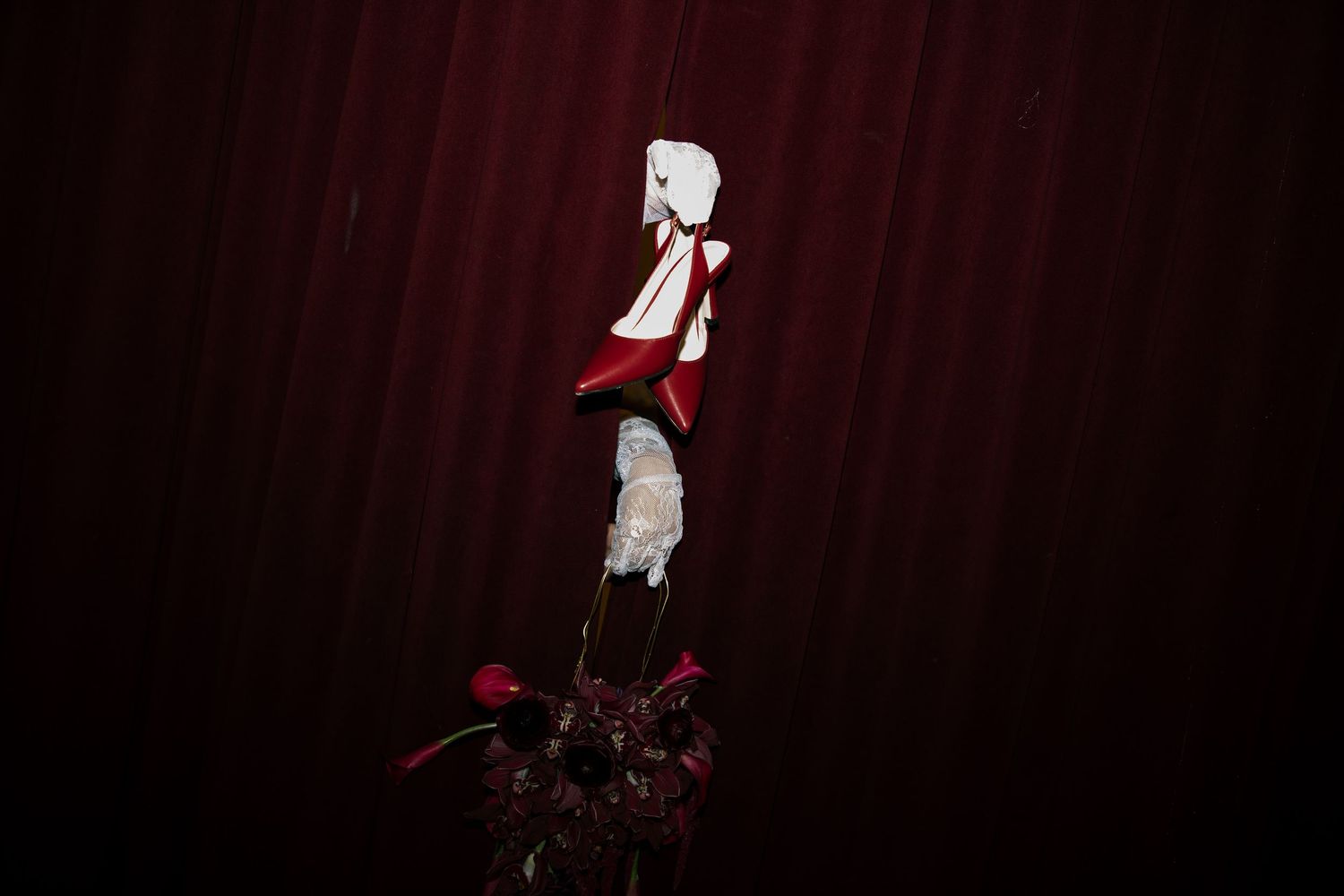 A white puppet figure in red and white costume displayed on a pole against a dark red curtain backdrop.