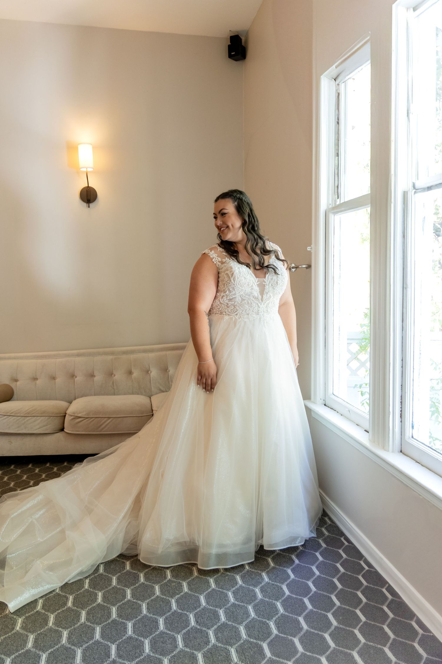 Elegant bridal portrait showing a flowing white wedding gown near a bright window.