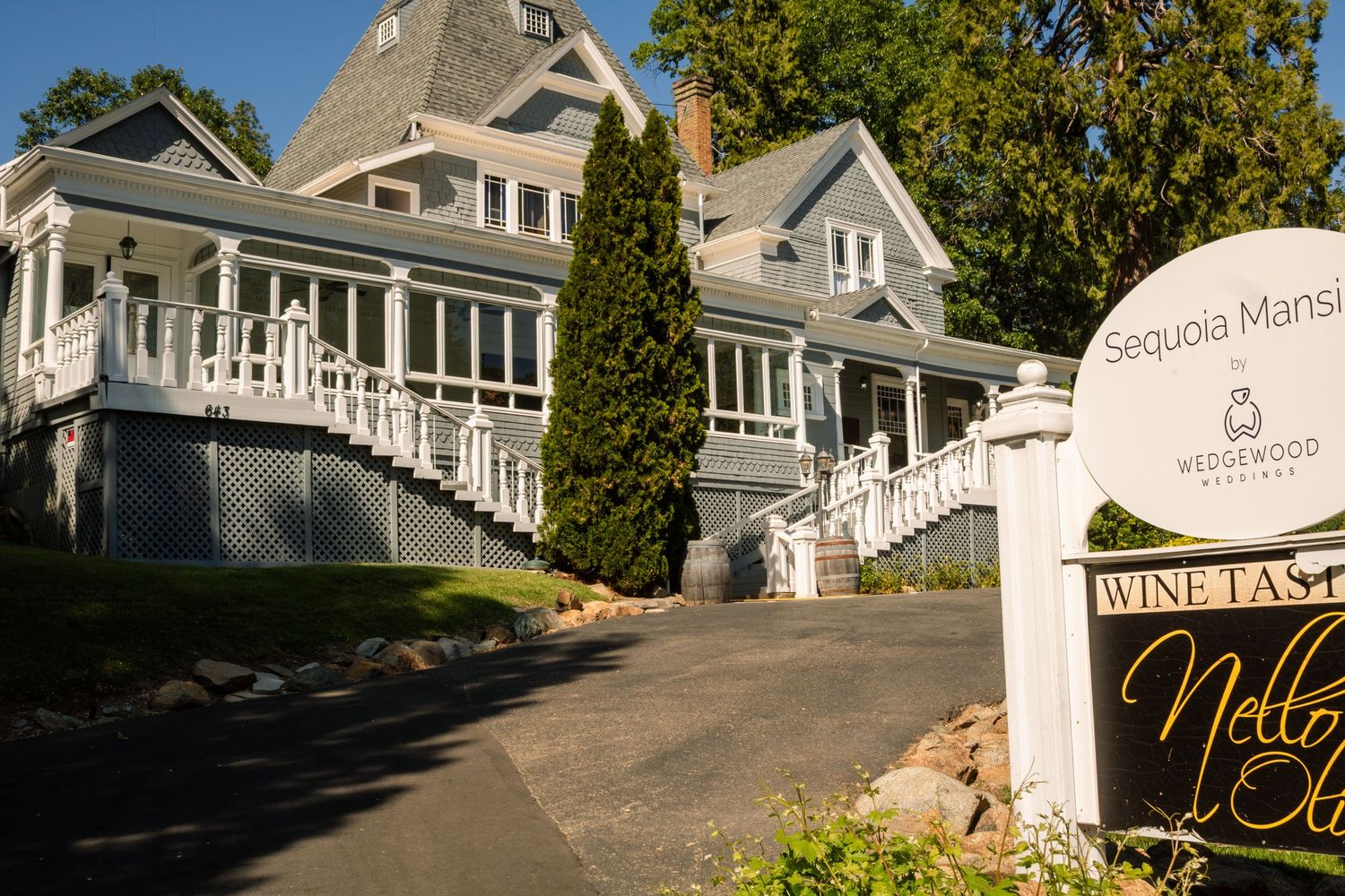 Elegant Victorian-style mansion with white trim and wraparound porch serving as a wine tasting venue.