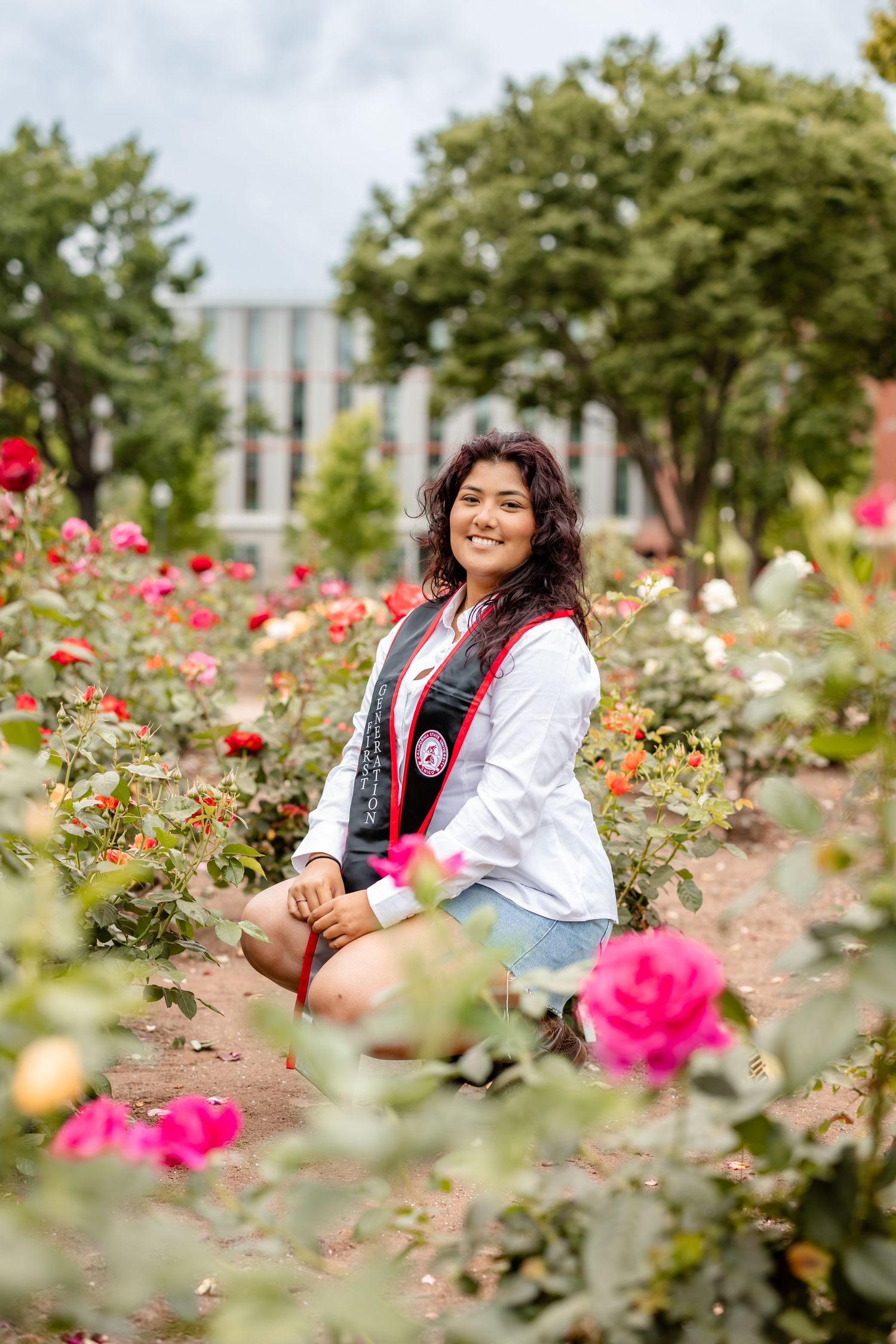 Portrait session in a rose garden with bright pink flowers in the foreground.