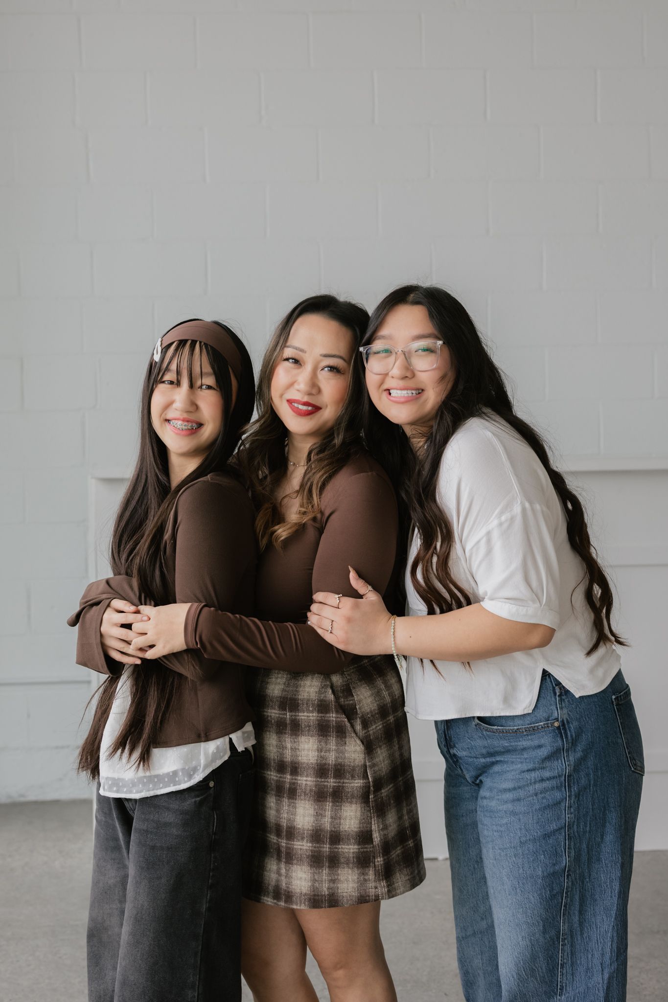Three friends in casual outfits pose together against a light gray wall in a series of candid photos.