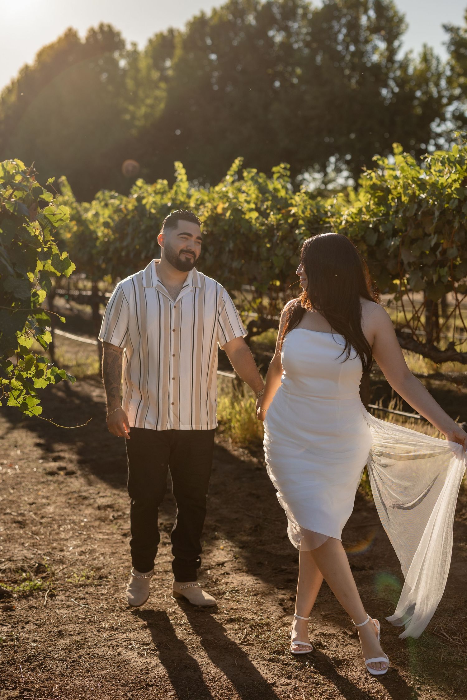 A couple dances together in a sun-lit vineyard during sunset.