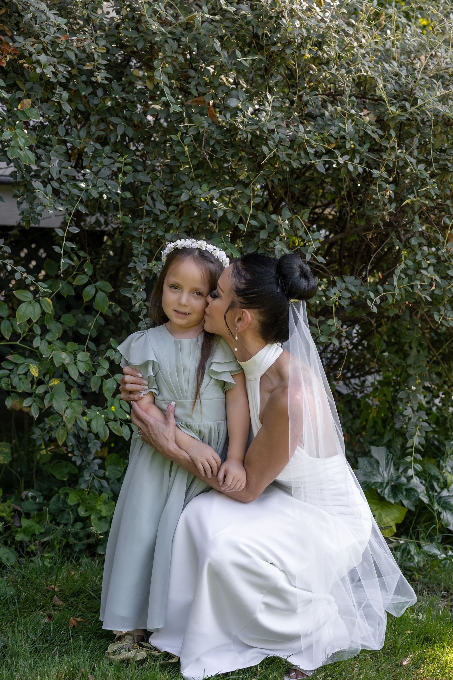 Sweet moment between bride and flower girls in a garden setting.