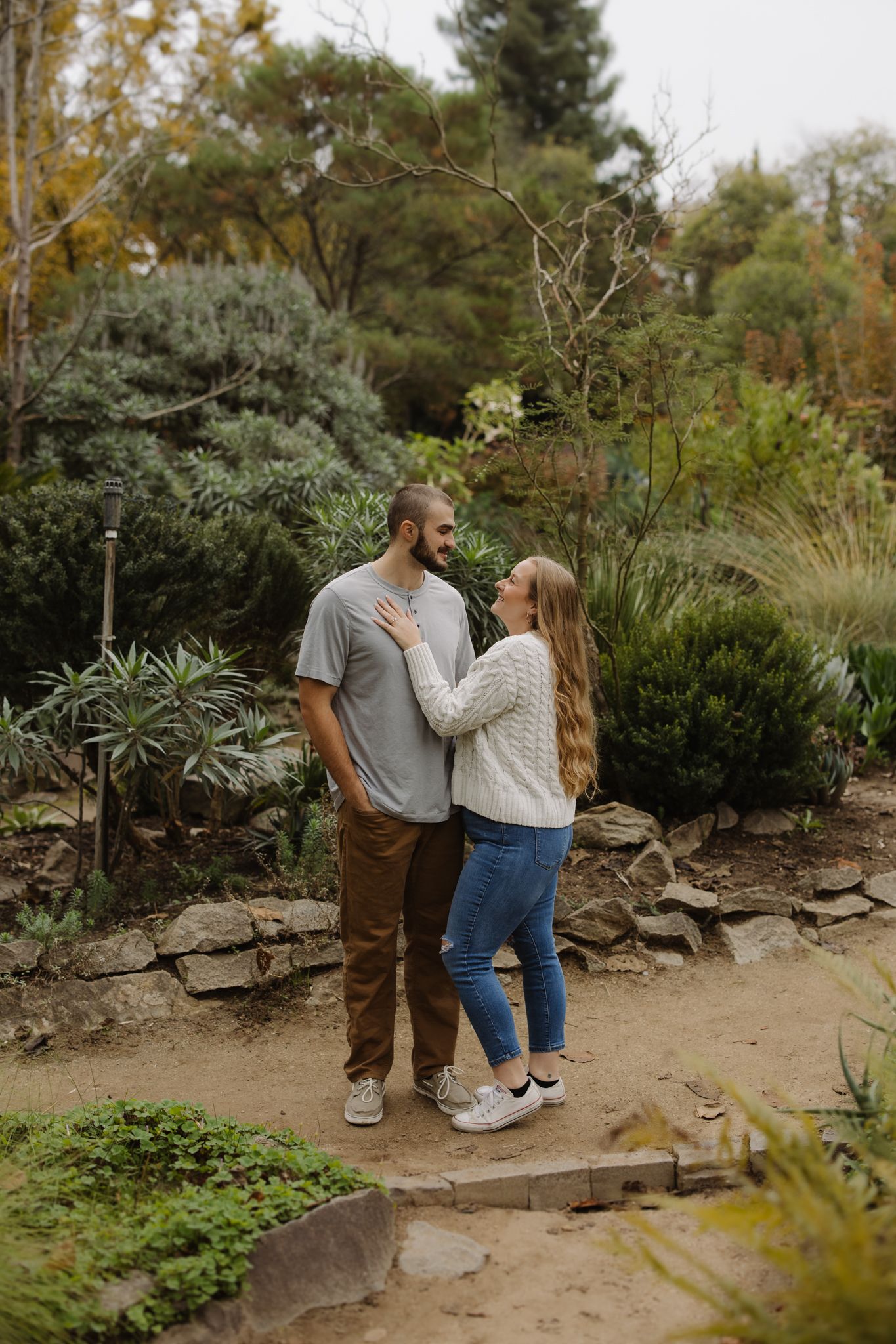 A couple shares romantic moments in a garden setting with lush greenery and stone pathways.