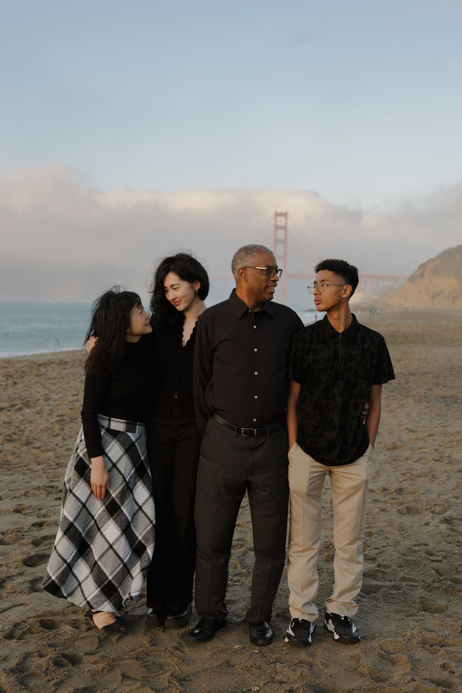 A group of people standing together on a beach with the Golden Gate Bridge visible in the background.