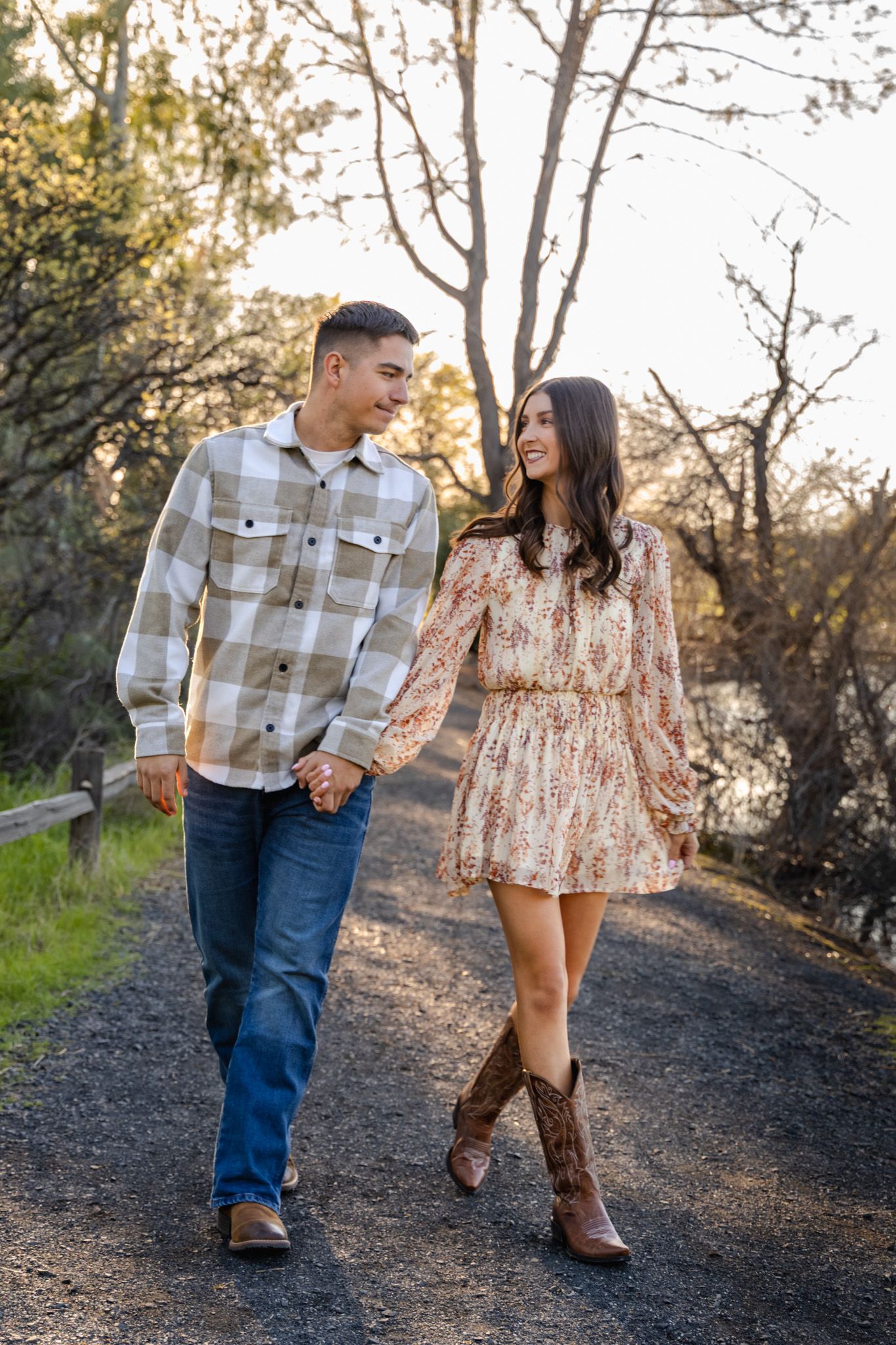 A couple walks hand in hand along a nature trail during golden hour.