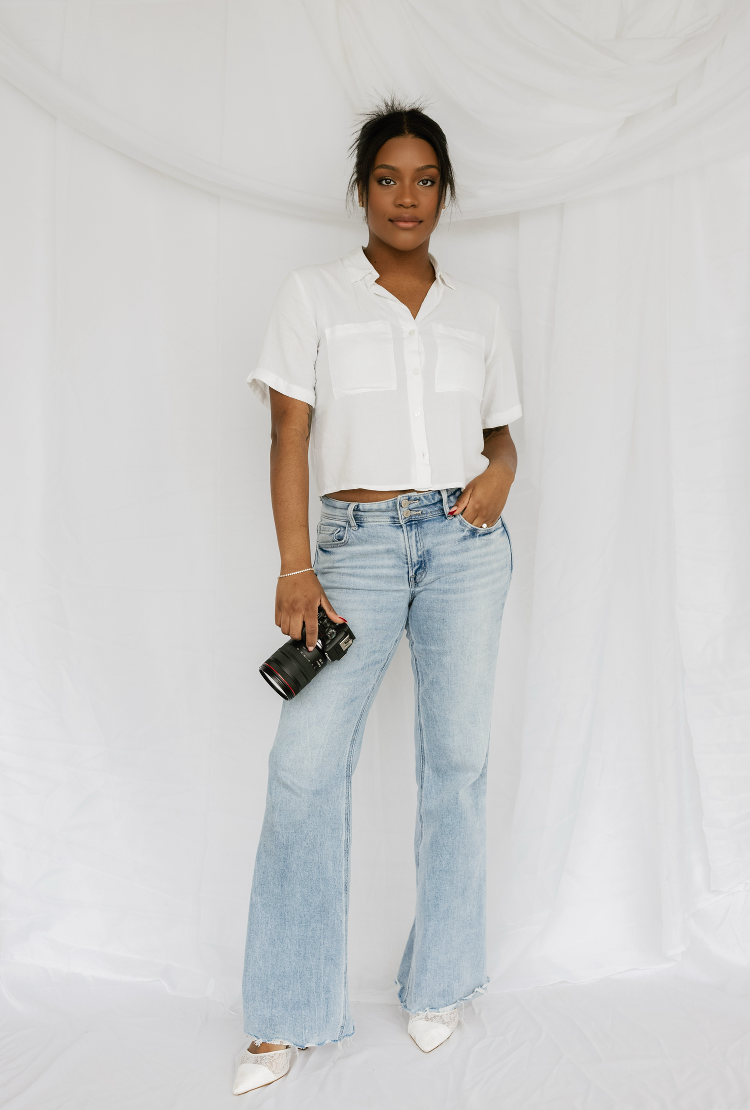 A casual fashion look featuring light wash wide leg jeans paired with a white cropped top against a white backdrop.