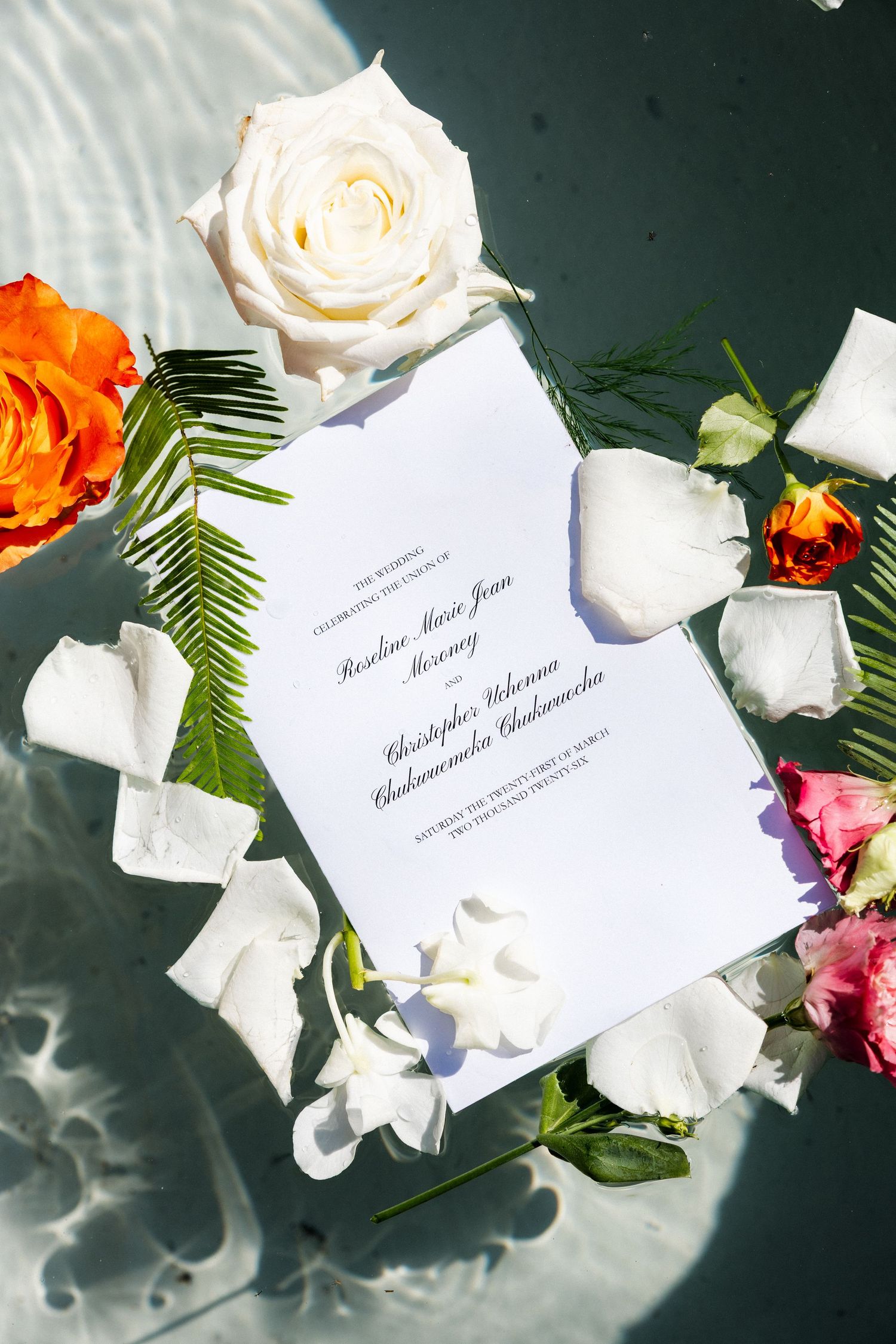 Wedding invitation cards surrounded by white roses and colorful flowers on a dark surface with dramatic lighting.