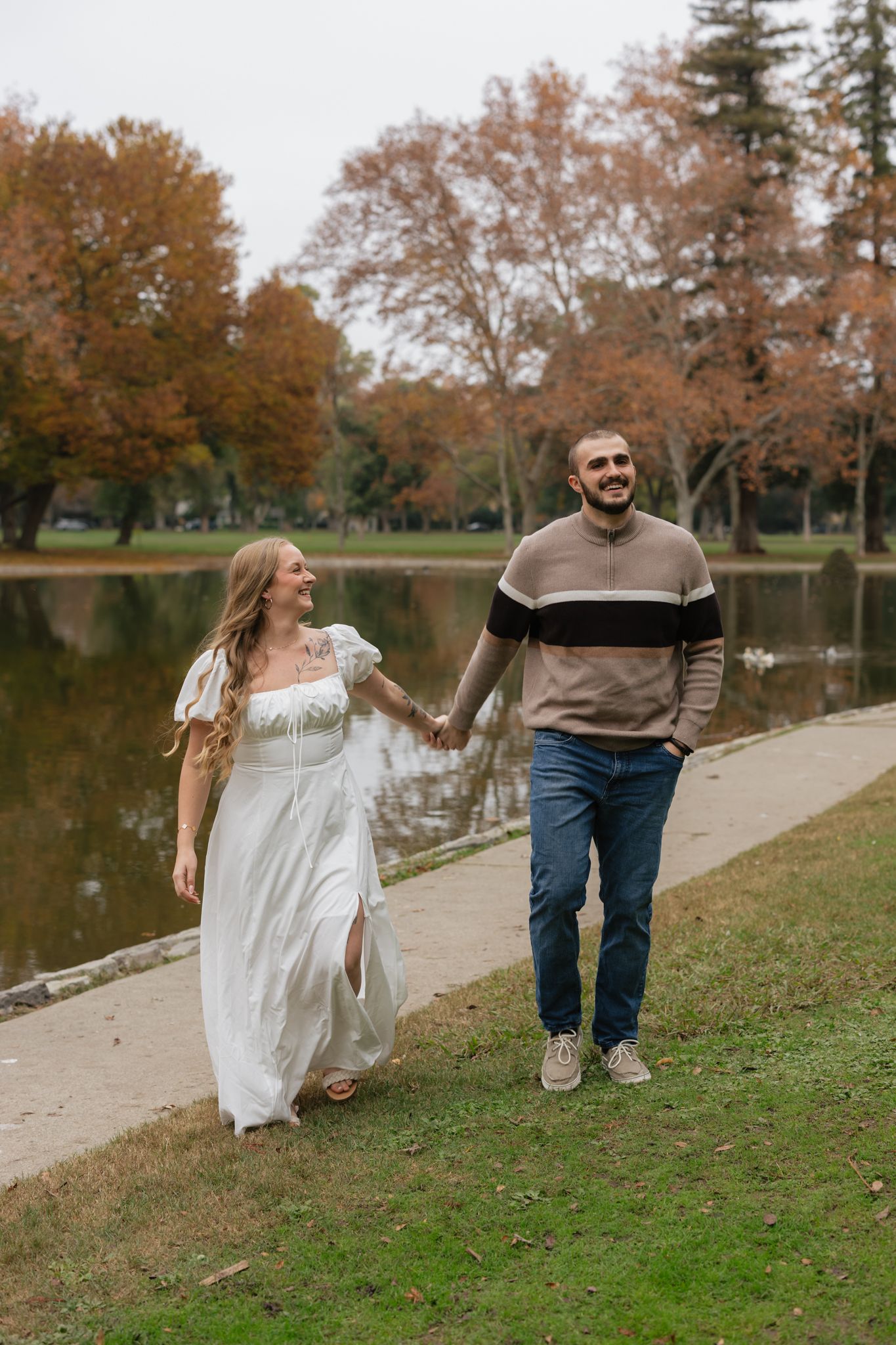 Playful autumn photoshoot by a lake with fall foliage in the background.