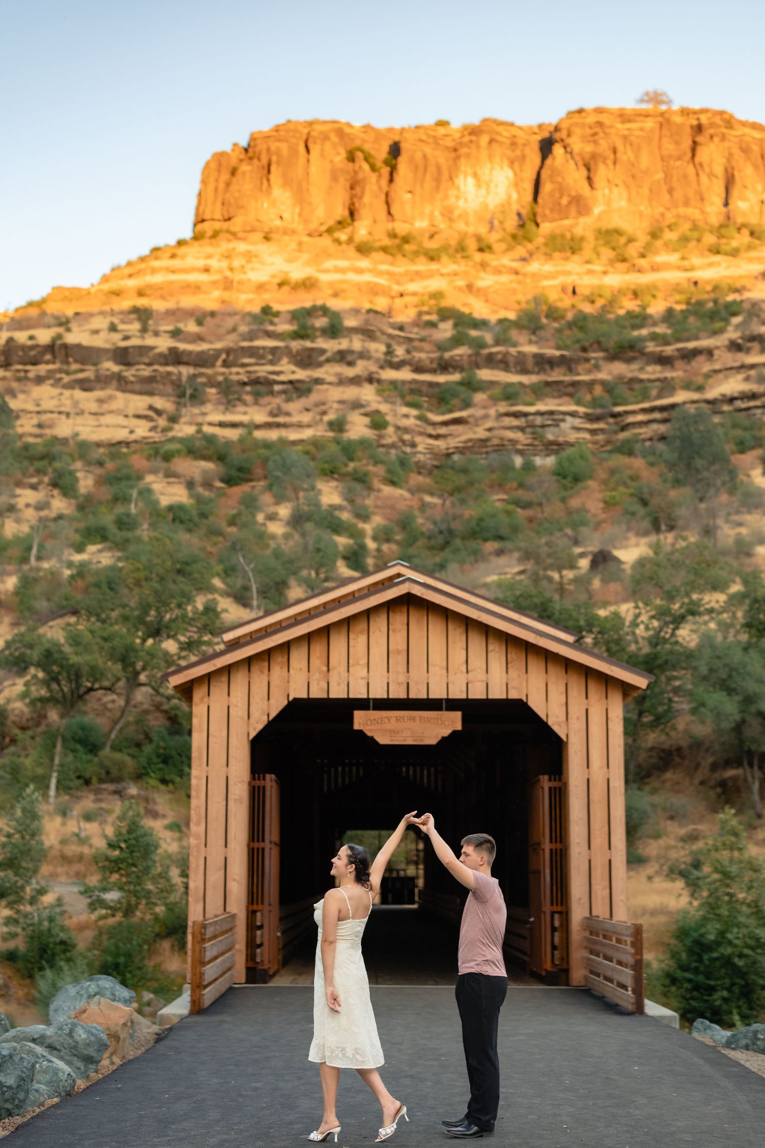 A couple dancing and twirling in front of a rustic wooden structure with red rock cliffs in the background.