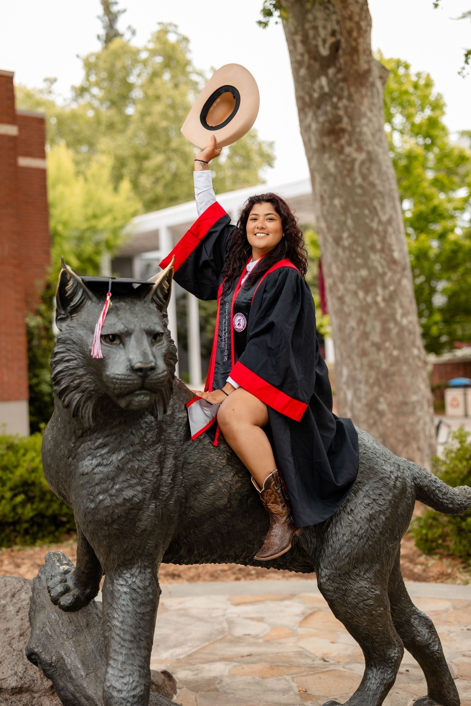 Graduate poses playfully on black panther statue in graduation cap and gown.