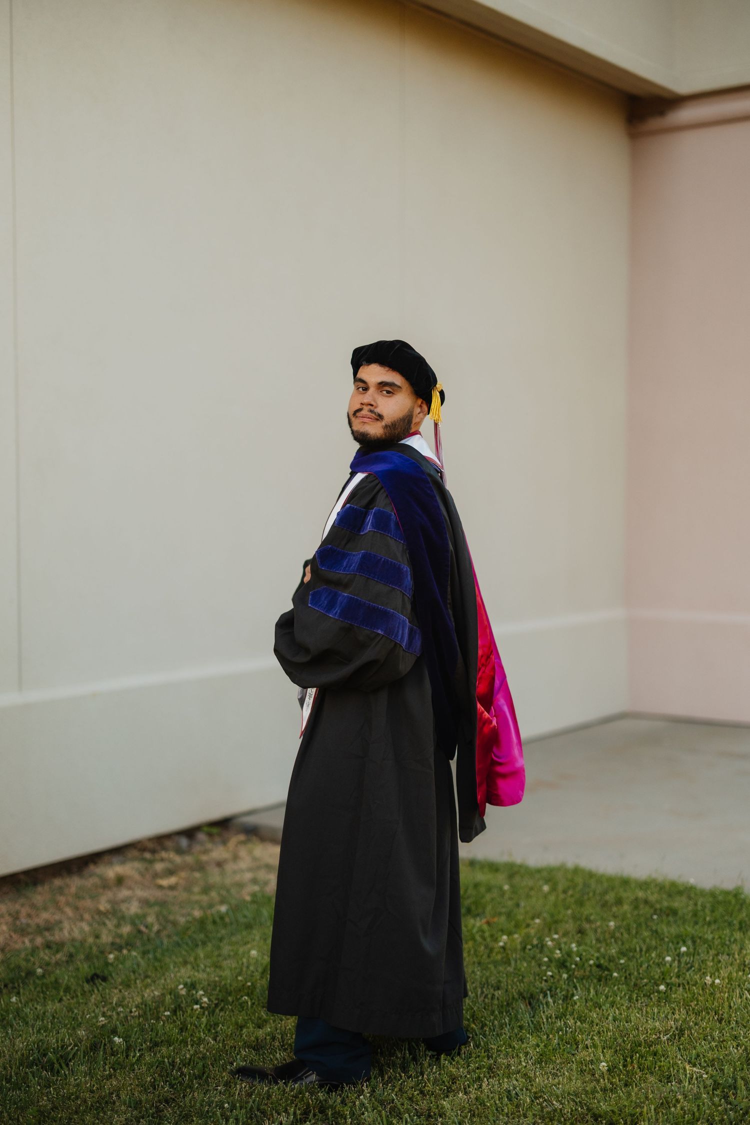 Graduate in academic regalia poses near campus building.