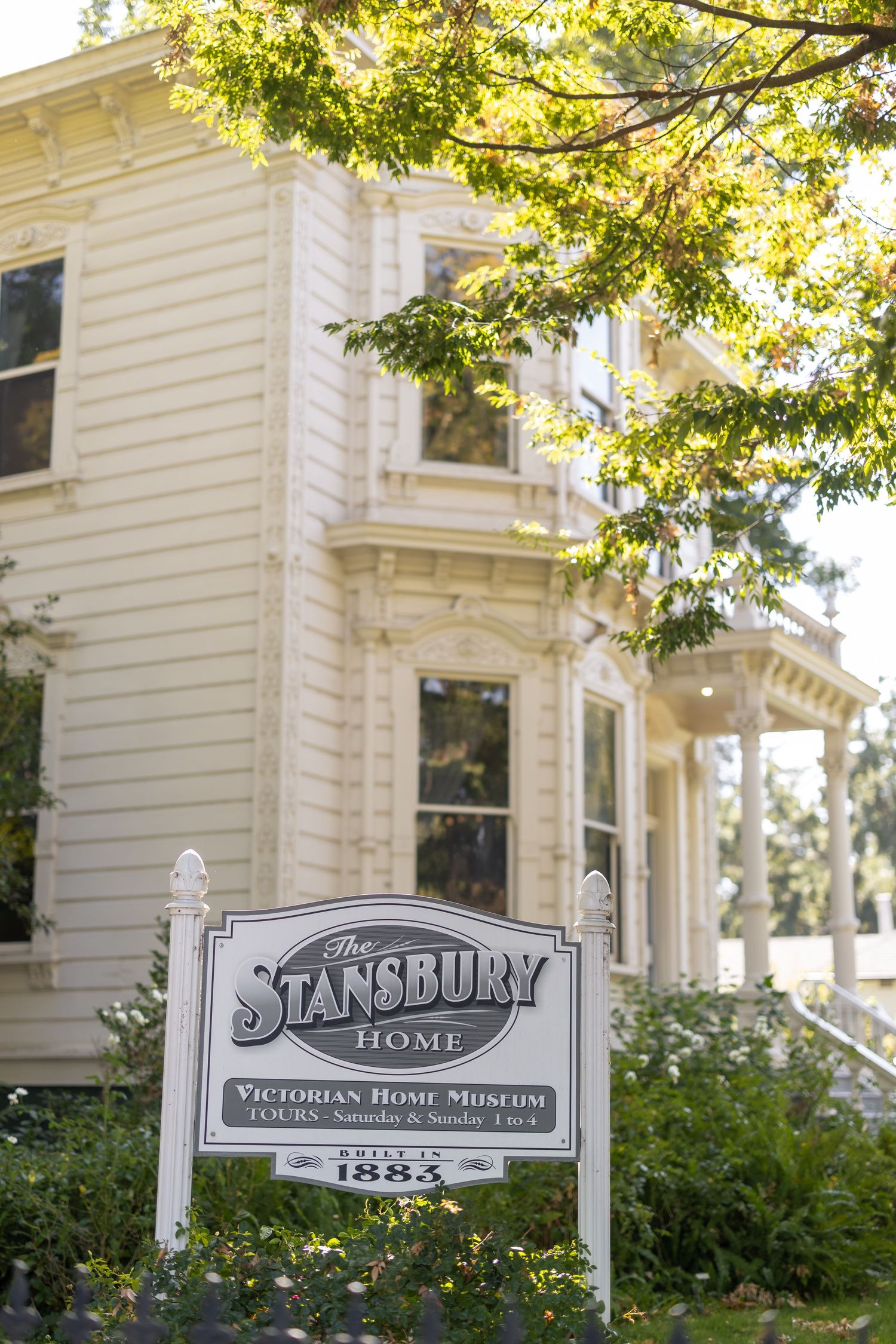 White Victorian mansion exterior with signs for Stansbury Home Victorian House Museum.