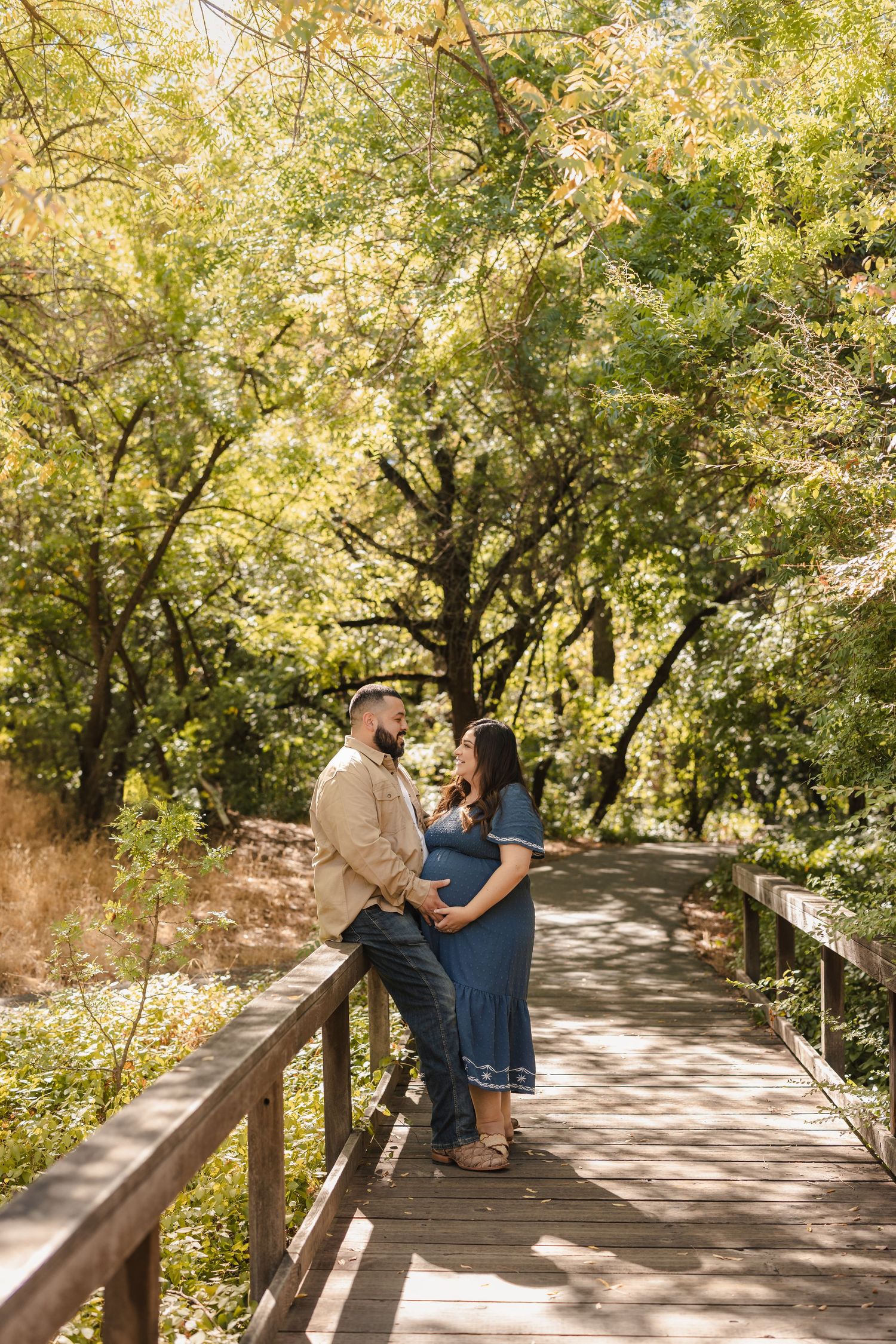 A couple sitting together on a wooden bridge path surrounded by lush green trees.