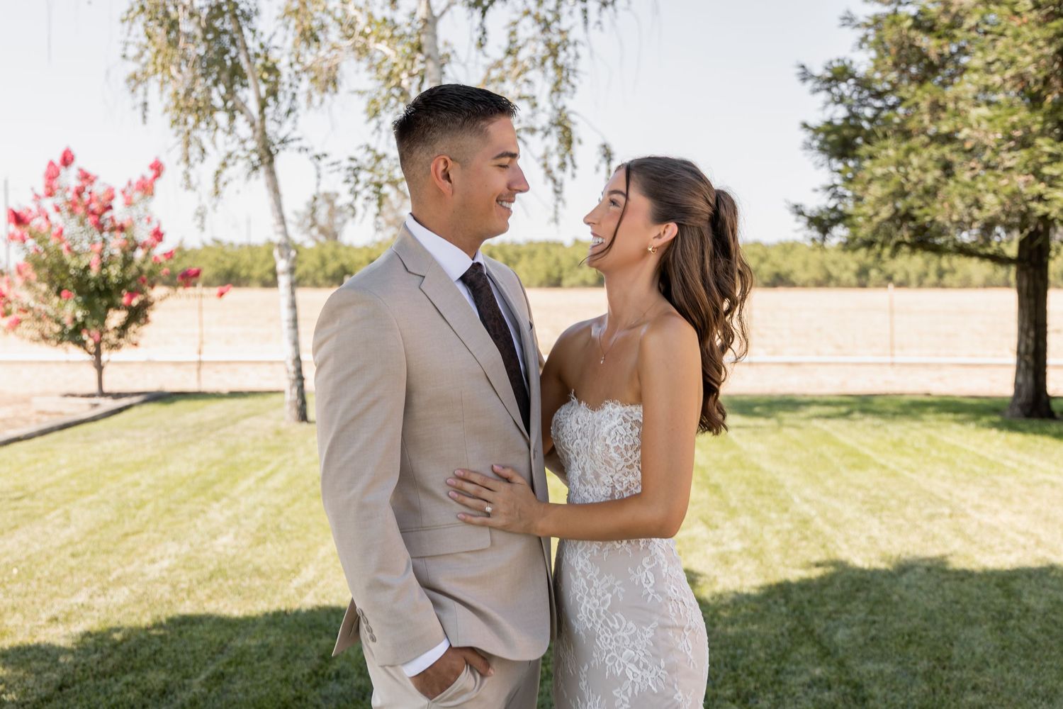 Couple in wedding attire embracing on sunny lawn.