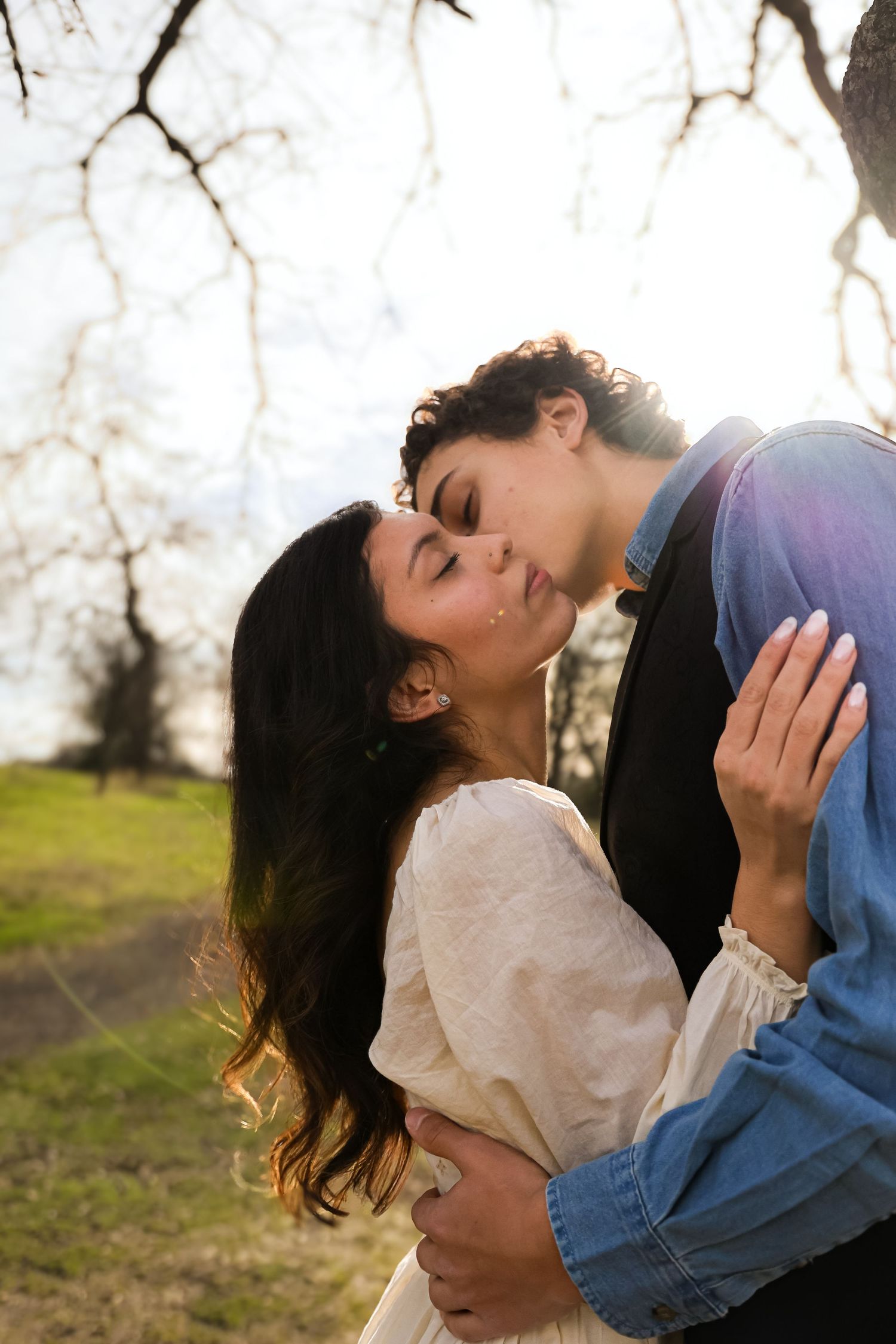 Romantic couple embracing in sunlit natural setting.