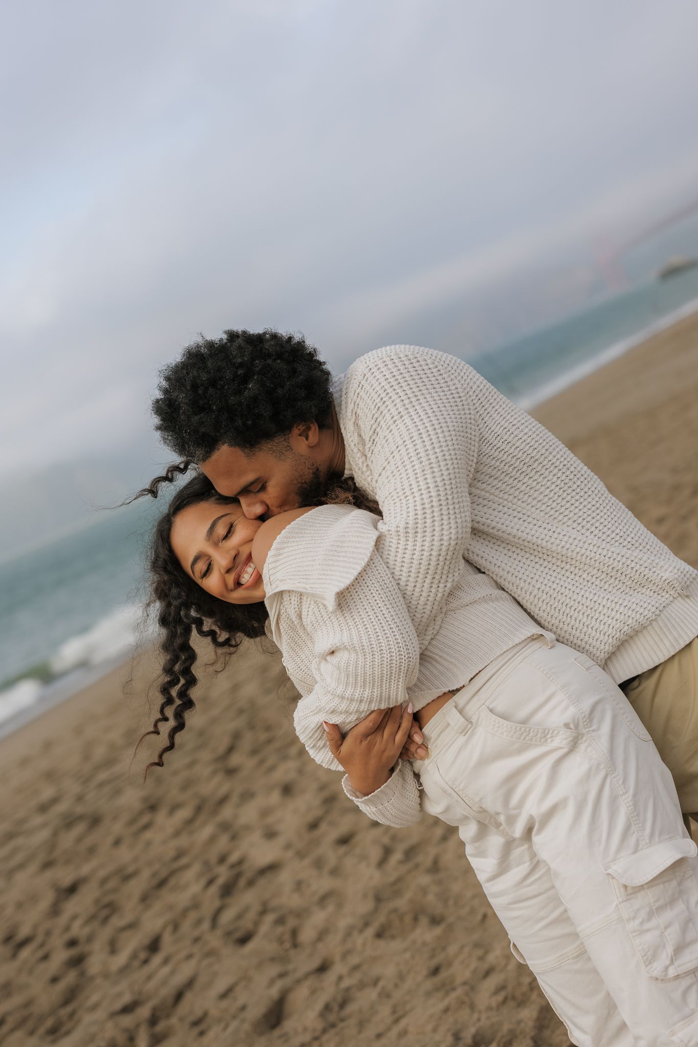 A romantic photoshoot sequence at the beach featuring warm knit sweaters and white outfits against a cloudy sky.