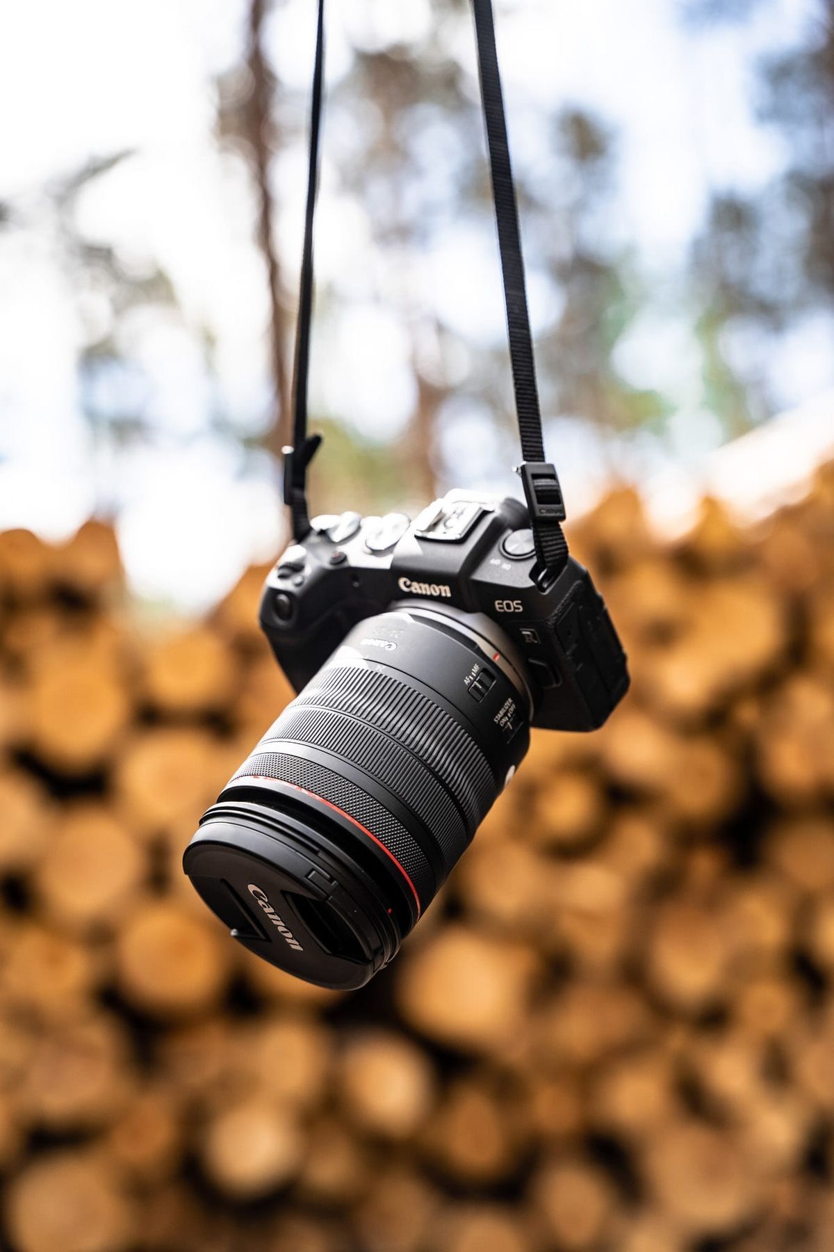 A Canon camera with telephoto lens hanging against a blurred orange background.