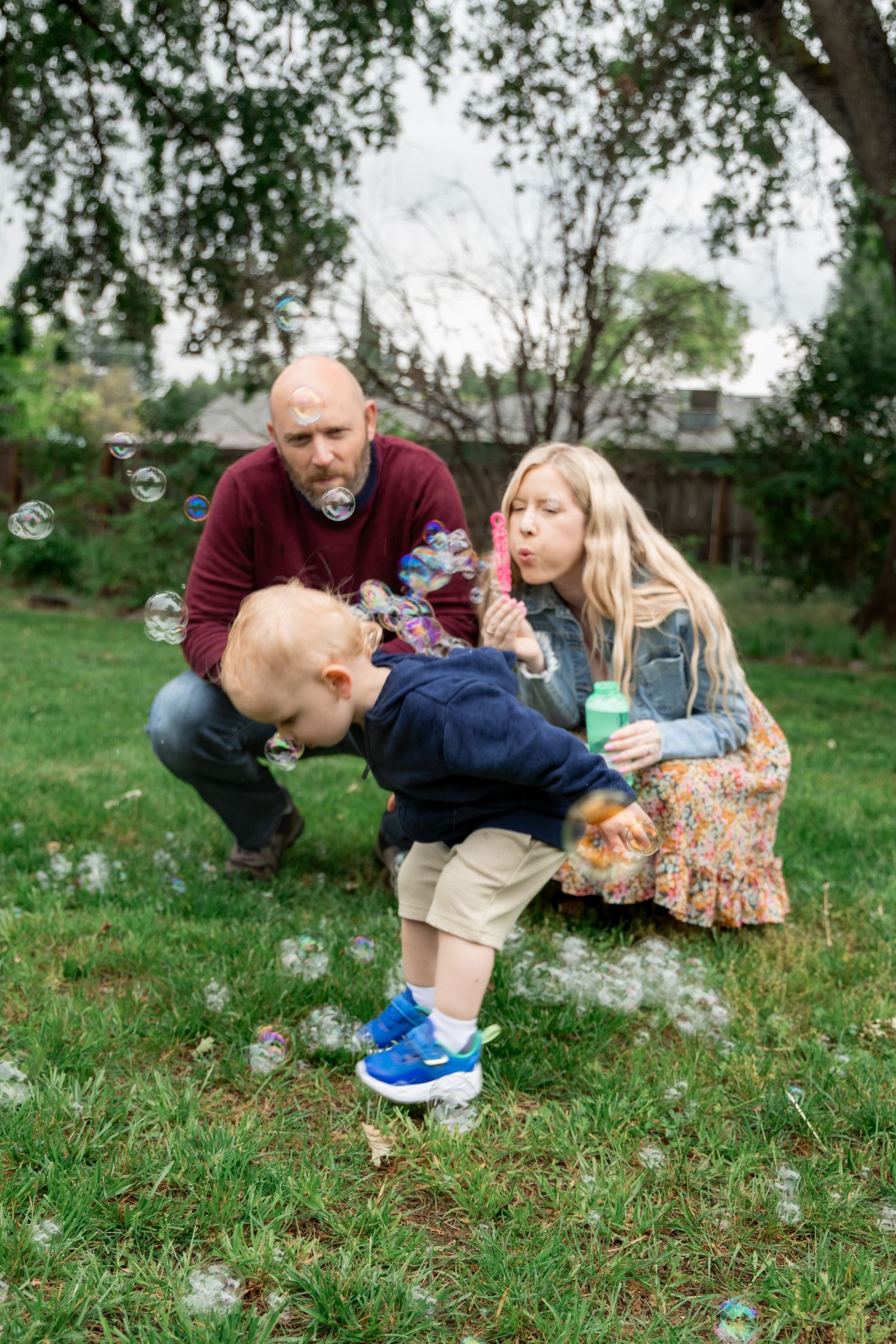 Playful family blowing dandelions together on grassy hill during spring.
