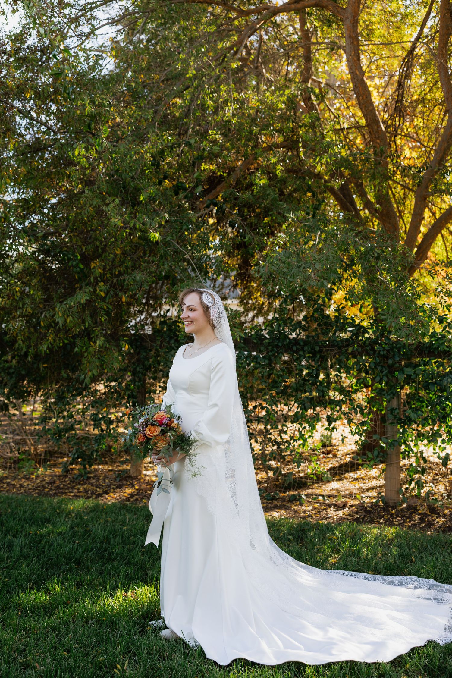 Elegant bridal portrait in a garden setting with long train dress and autumn foliage.