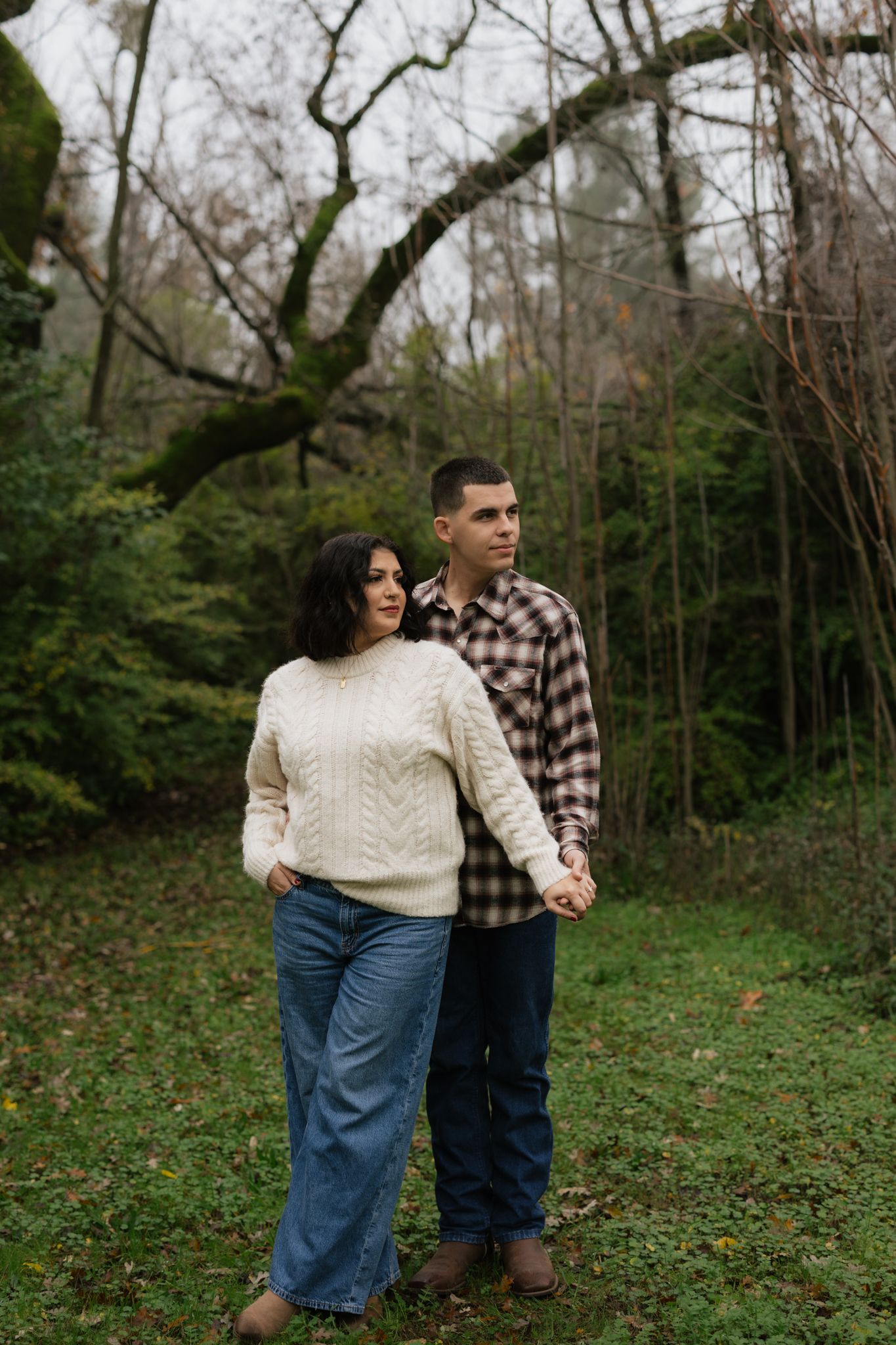 Couple in matching casual wear standing in wooded area.