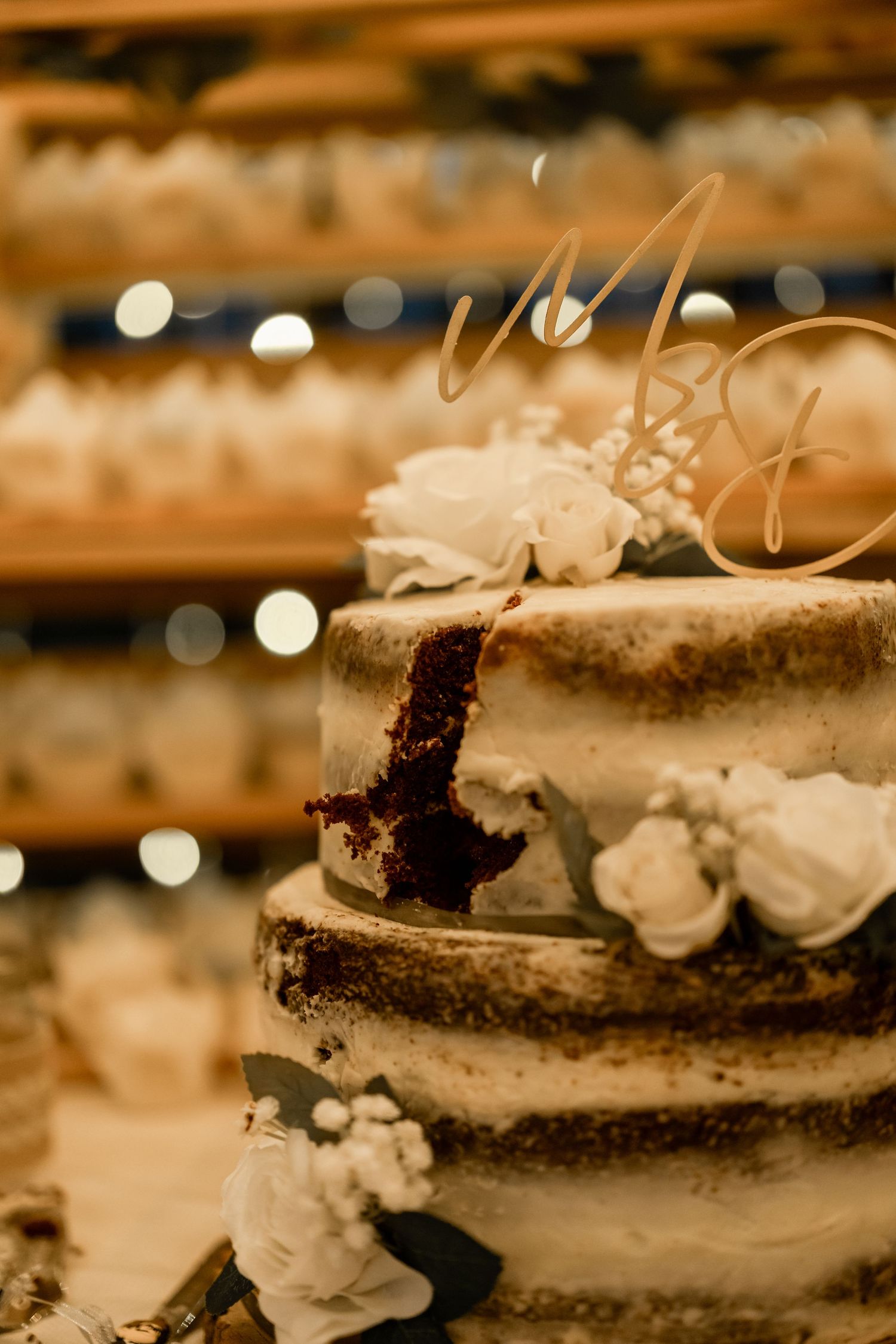 Close-up of elegant naked wedding cake with white floral decorations and rustic details.