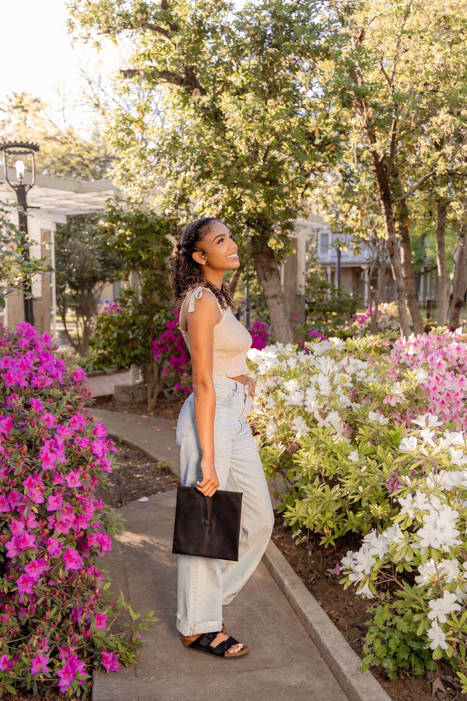 Person in white outfit admires colorful flowers in a garden path at sunset.