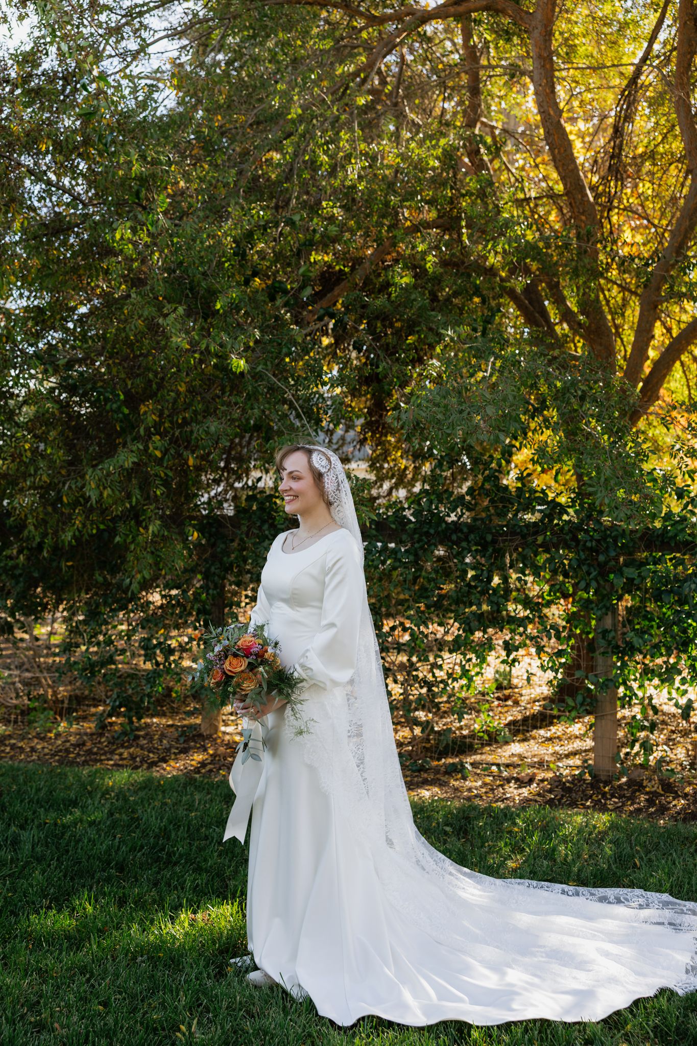 A beautiful bridal portrait in a sunlit garden setting with a flowing white wedding gown and delicate veil.