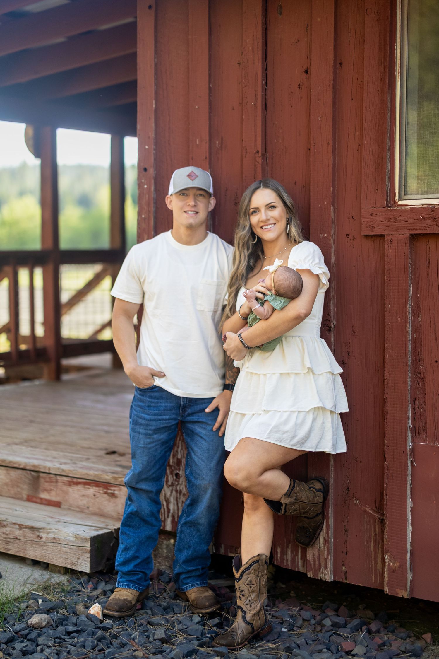 Couple poses together on a red barn porch wearing country western attire.