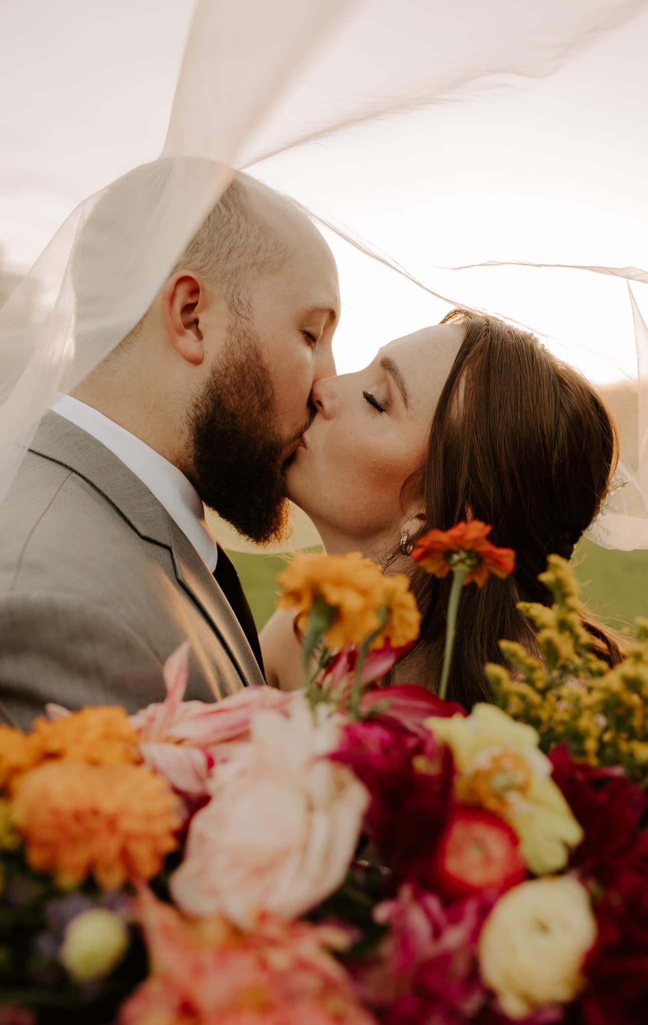 Wedding couple kissing with colorful floral arrangement in foreground.