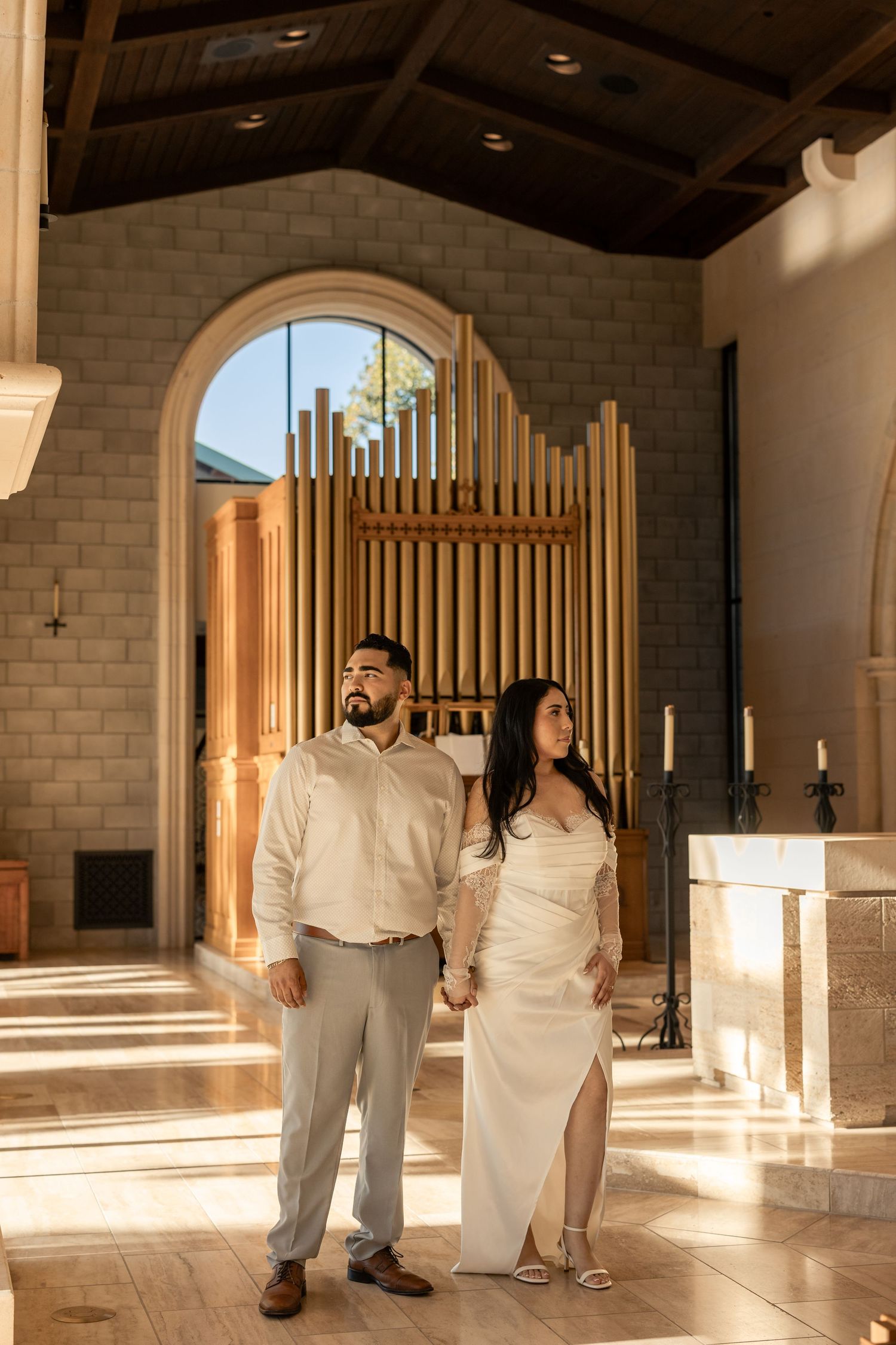 A couple poses in a sunlit church interior with wooden architectural details.