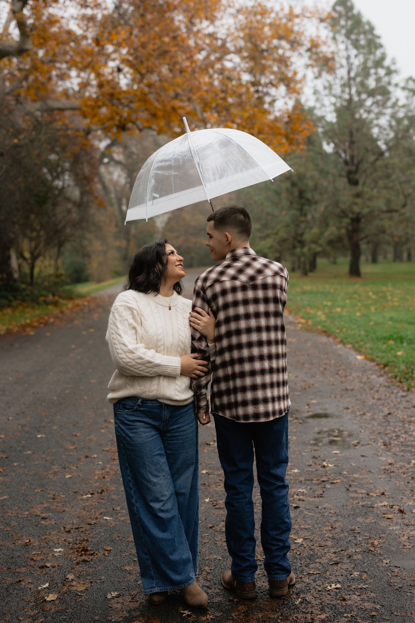 Couple sharing umbrella on autumn path with fallen leaves.