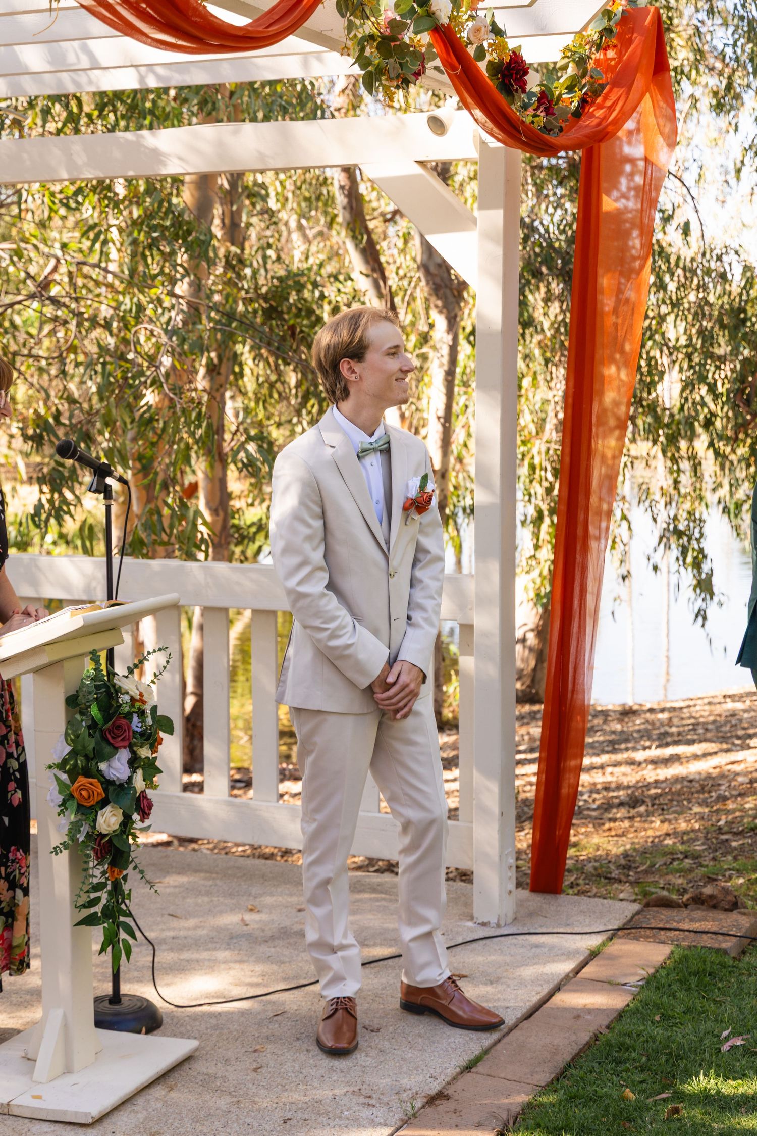 White gazebo decorated with orange fabric and floral arrangements for outdoor wedding ceremony.