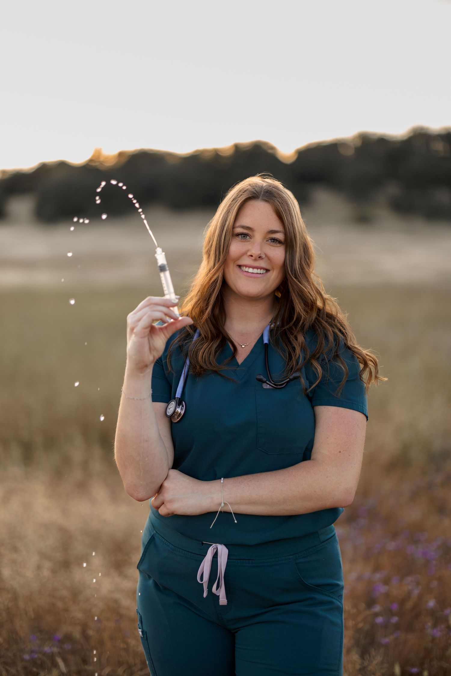 Person in navy scrubs celebrates with sparklers in a field at dusk.