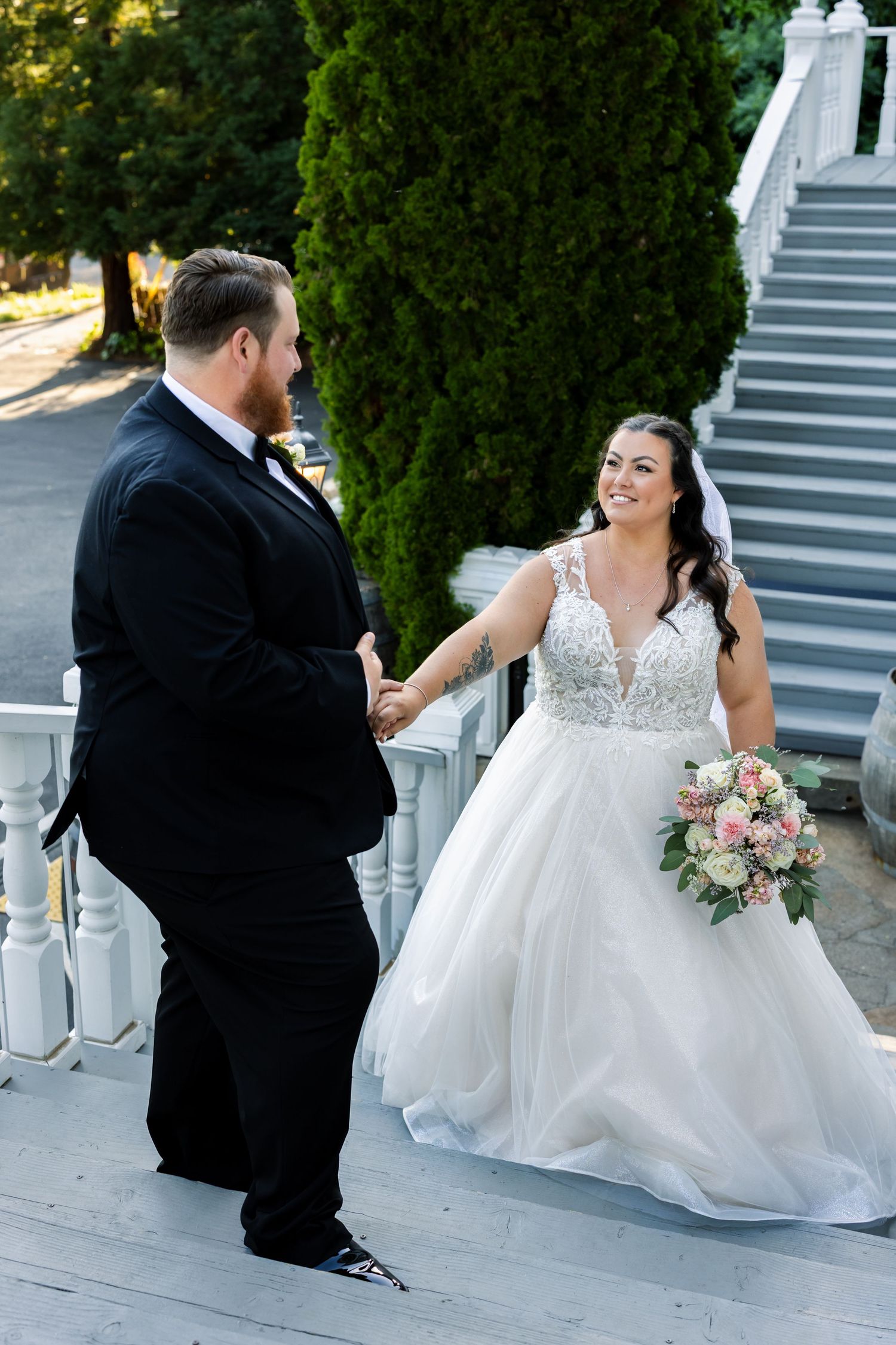 Sweet wedding moment captured on white porch stairs with bride holding pink bouquet.