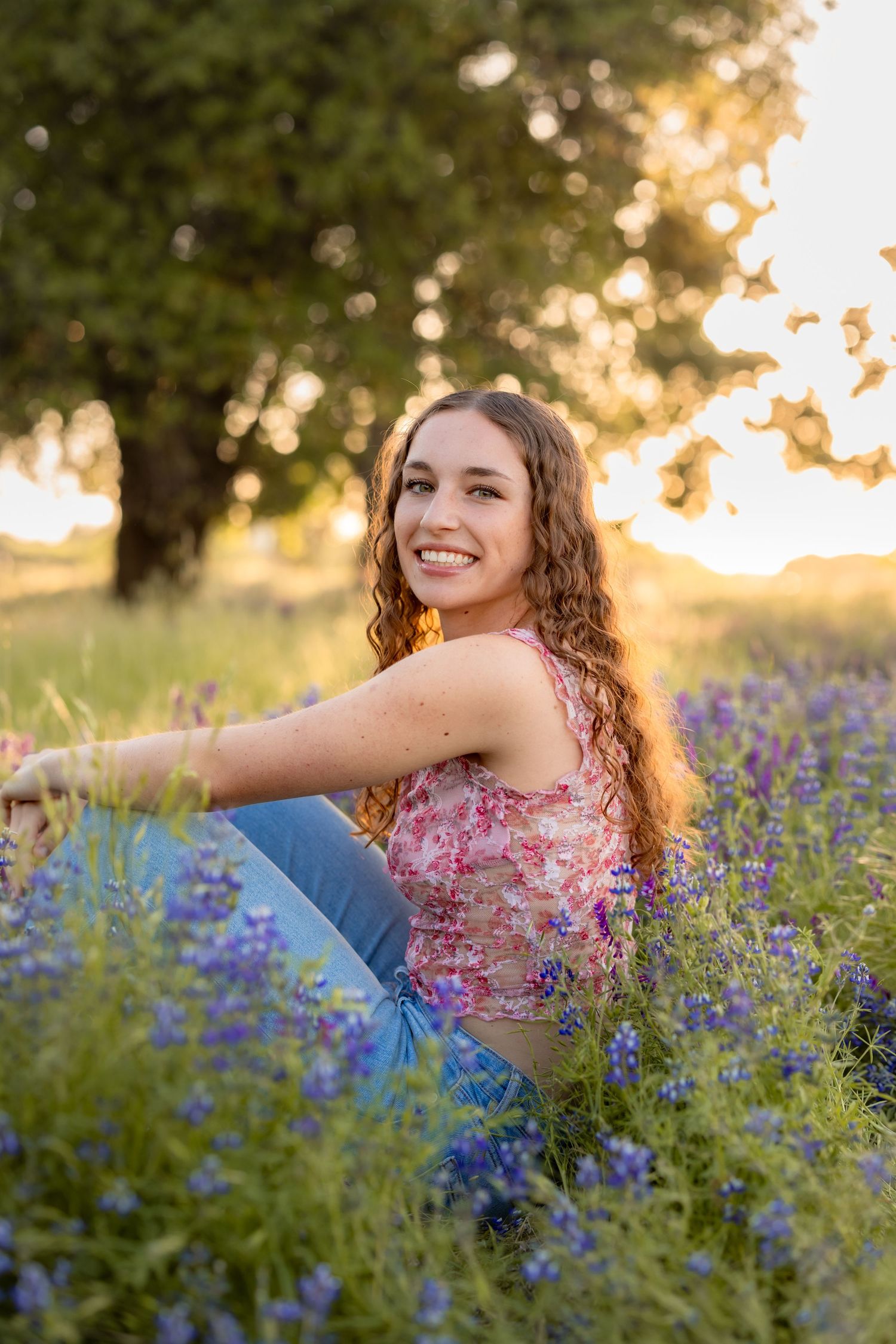 Woman in floral top poses in field of bluebonnets during golden hour.