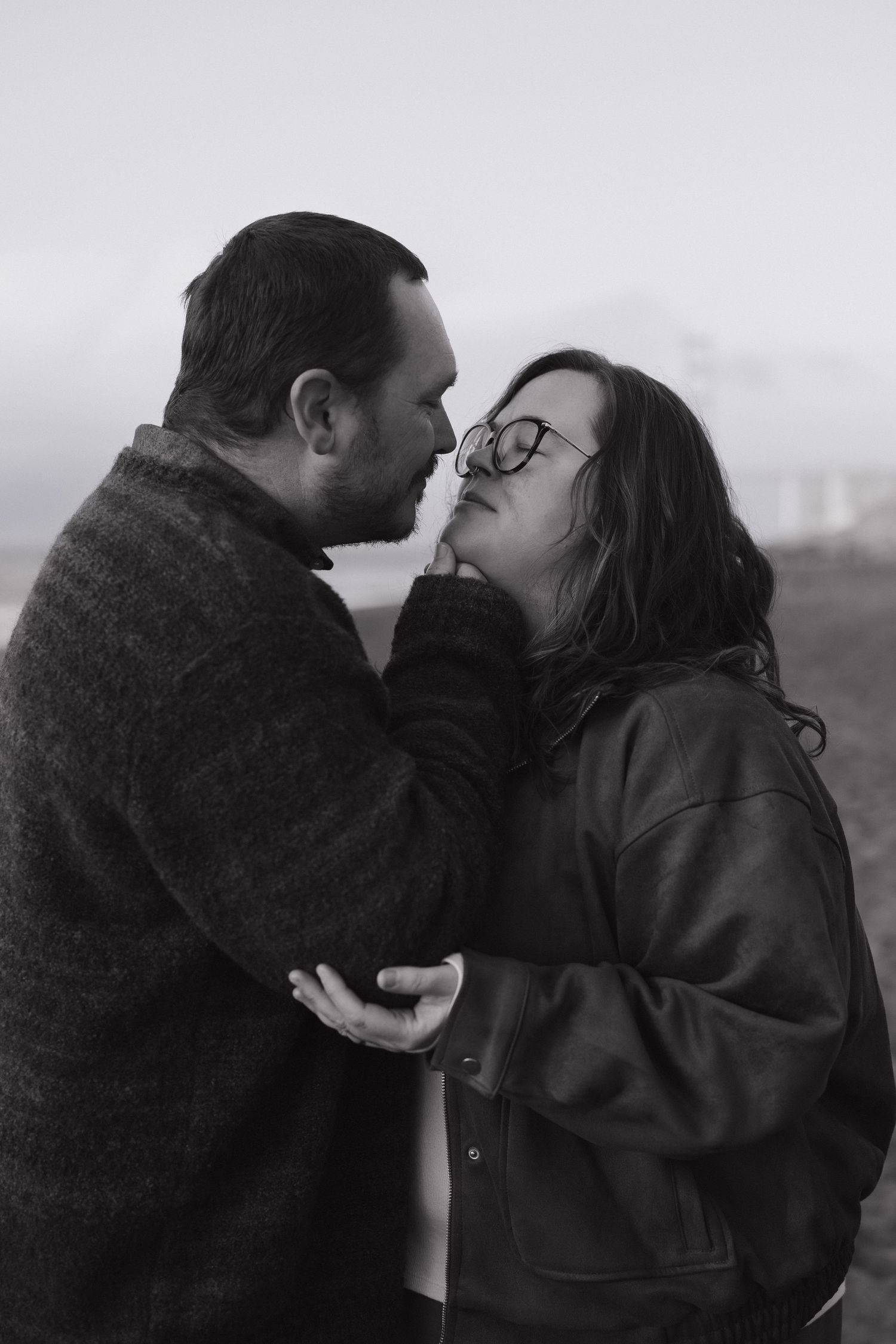 A romantic black and white portrait of a couple in winter coats sharing an intimate moment outdoors.